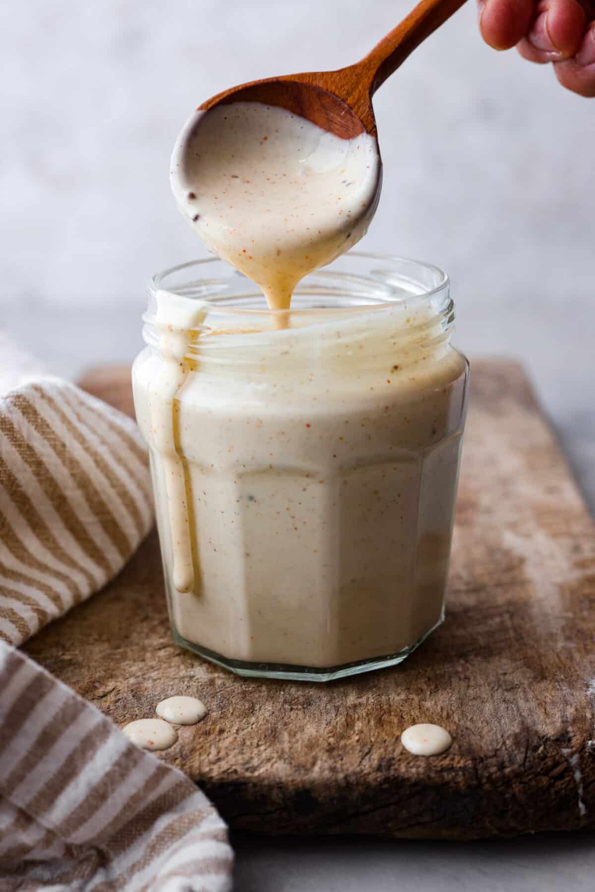 A jar of Alabama White BBQ Sauce with a wooden spoon scooping some out. 