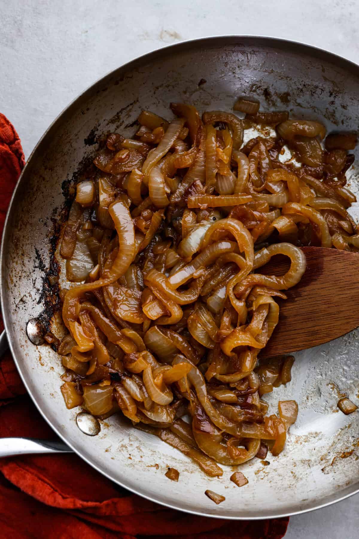 Caramelized onions being stirred with a wooden spoon in a metal pan.