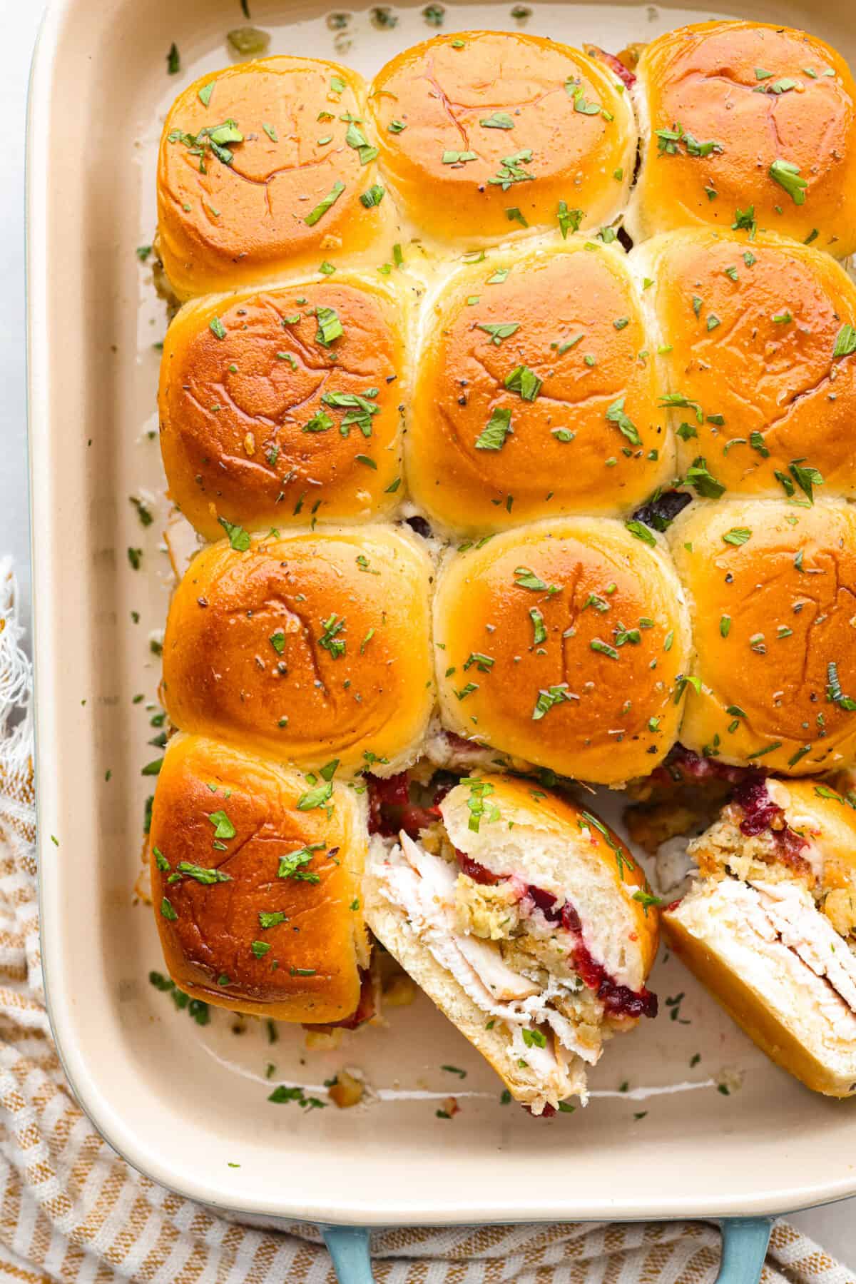 Top-down view of turkey cranberry sliders in a baking dish. Two are turned on their side so the filling can be seen.