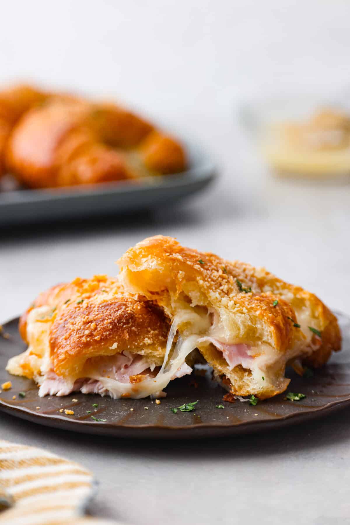 Close view of a ham and cheese croissant cut in half on a brown plate.