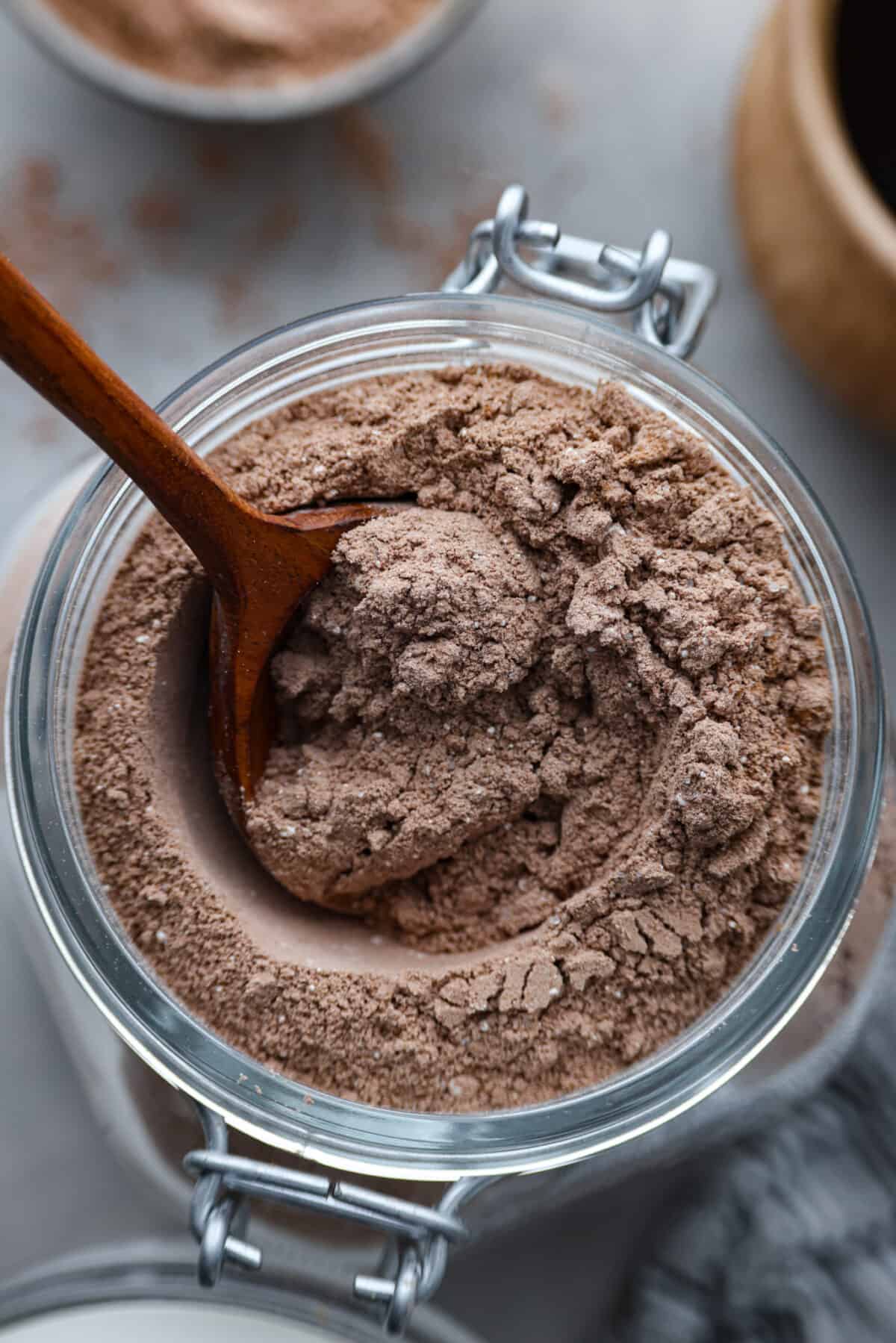 Top-down view of hot chocolate mix in a glass jar, being mixed with a wooden spoon.