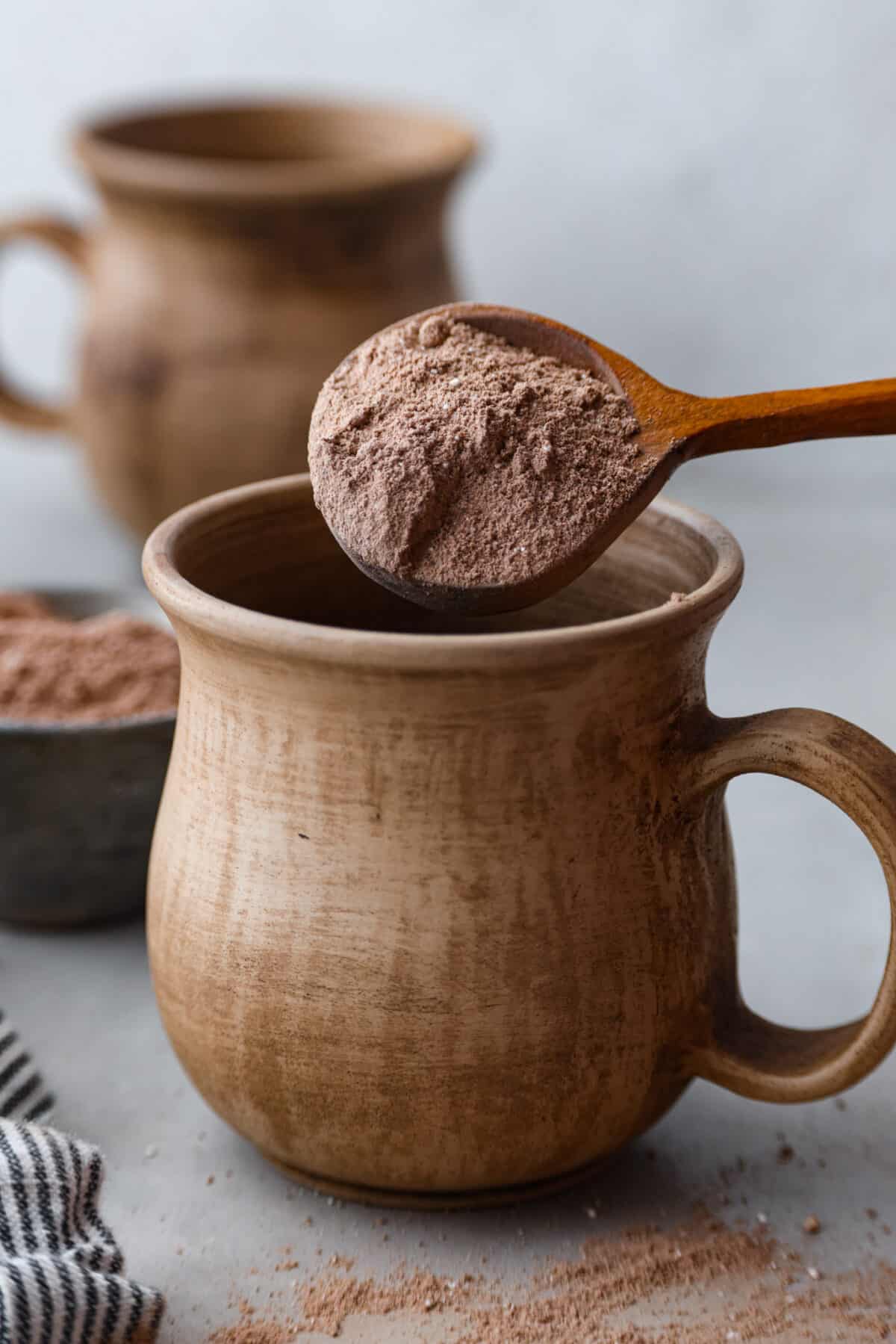 Pouring a spoonful of hot chocolate mix into a mug.
