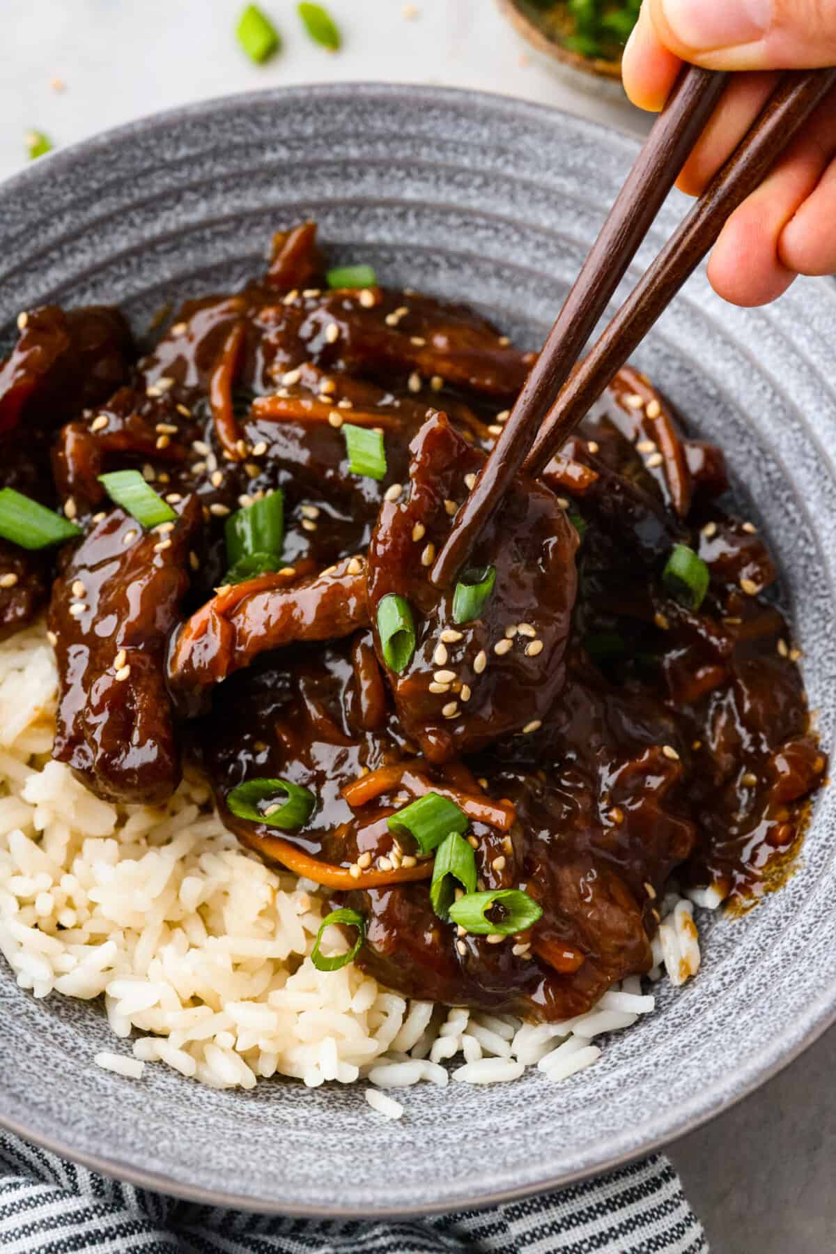 Close view of chopsticks lifting up whinge from a trencher of slow cooker Mongolian whinge over rice.