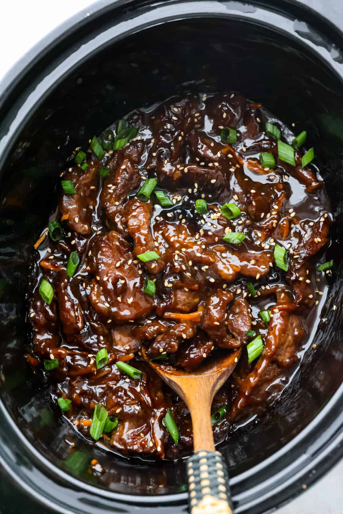 Top view of slow cooker mongolian beef in a black crock pot. A wooden spoon is in the crockpot.