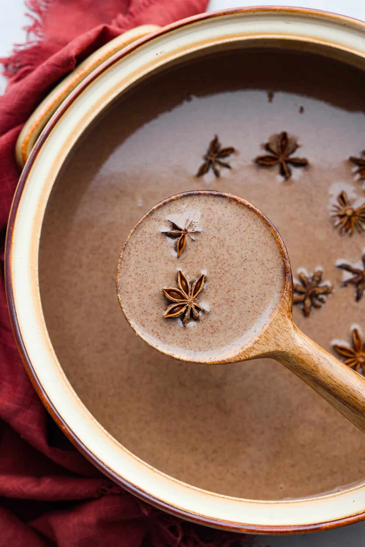 A pot of champurrado being served with a wooden ladle.