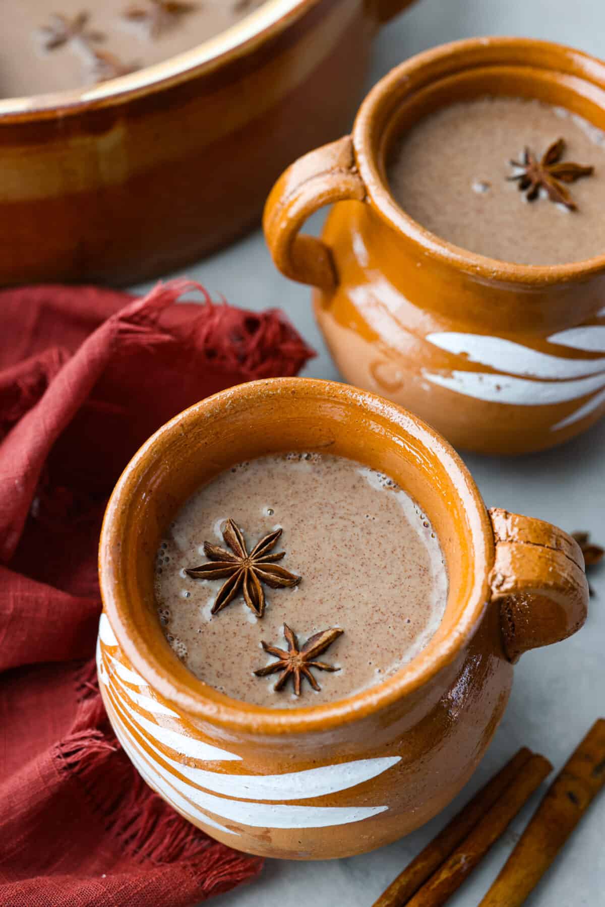 Champurrado in a brown mug. It's filled with star anise and surrounded with cinnamon sticks.