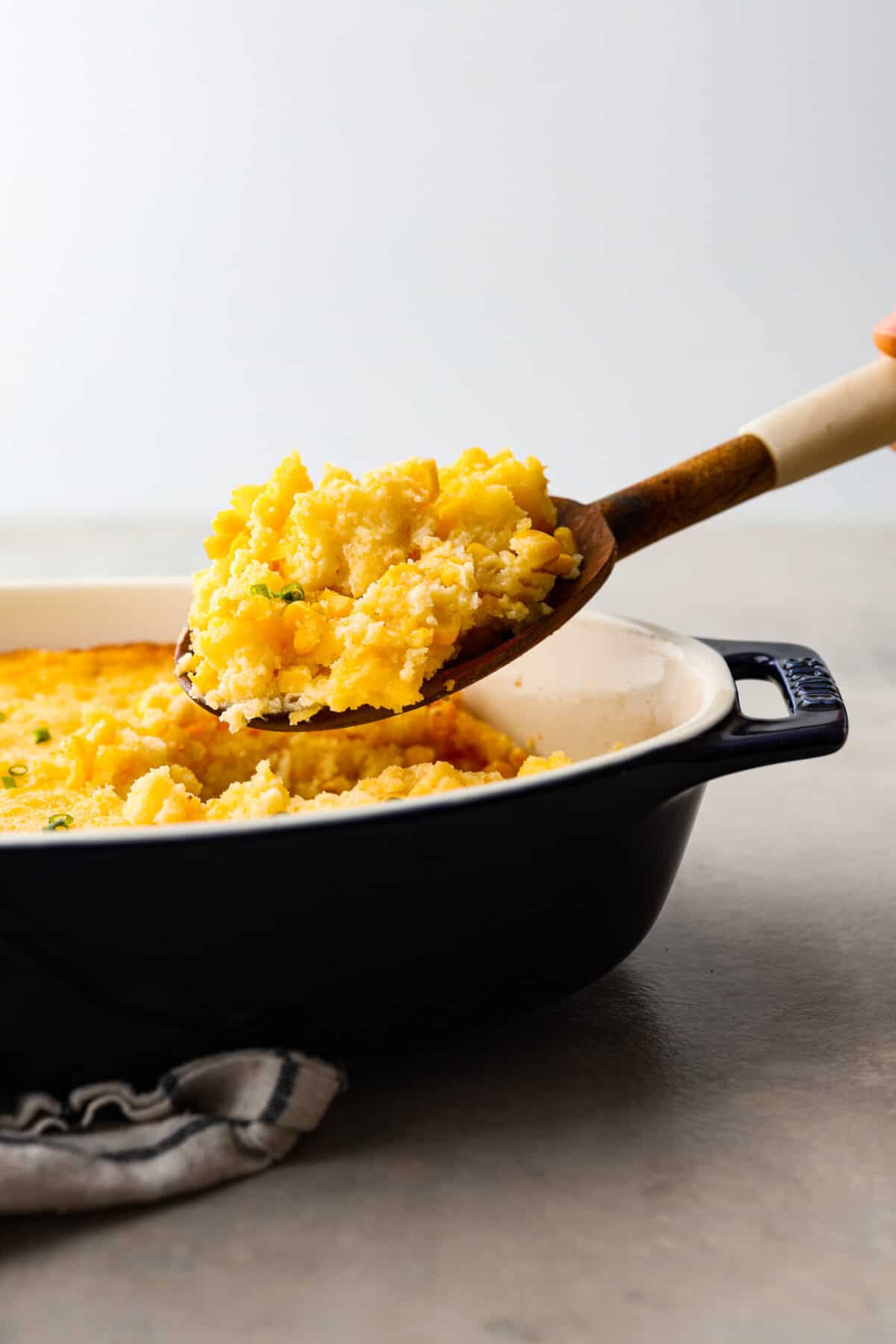 A scoop of corn casserole being taken out of the dish with a wooden spoon. 