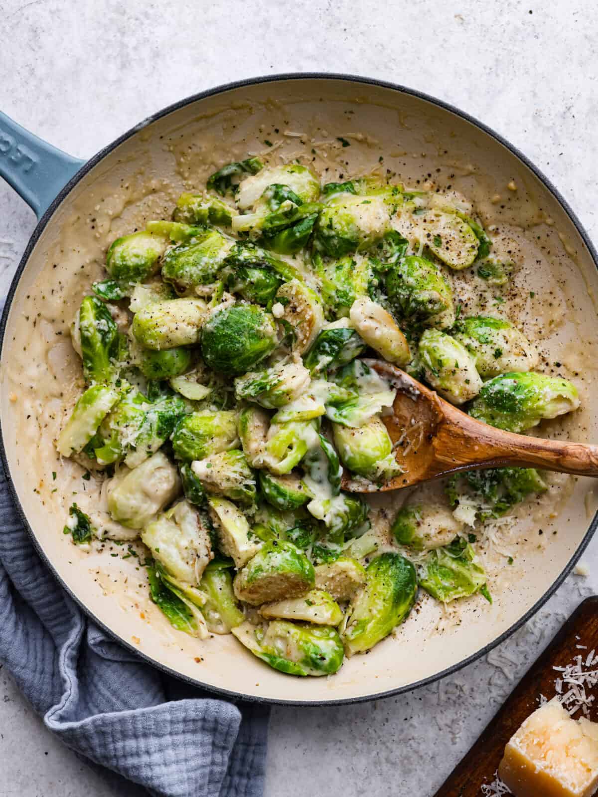 Top view of creamy brussels sprouts in a skillet with a wooden spoon.
