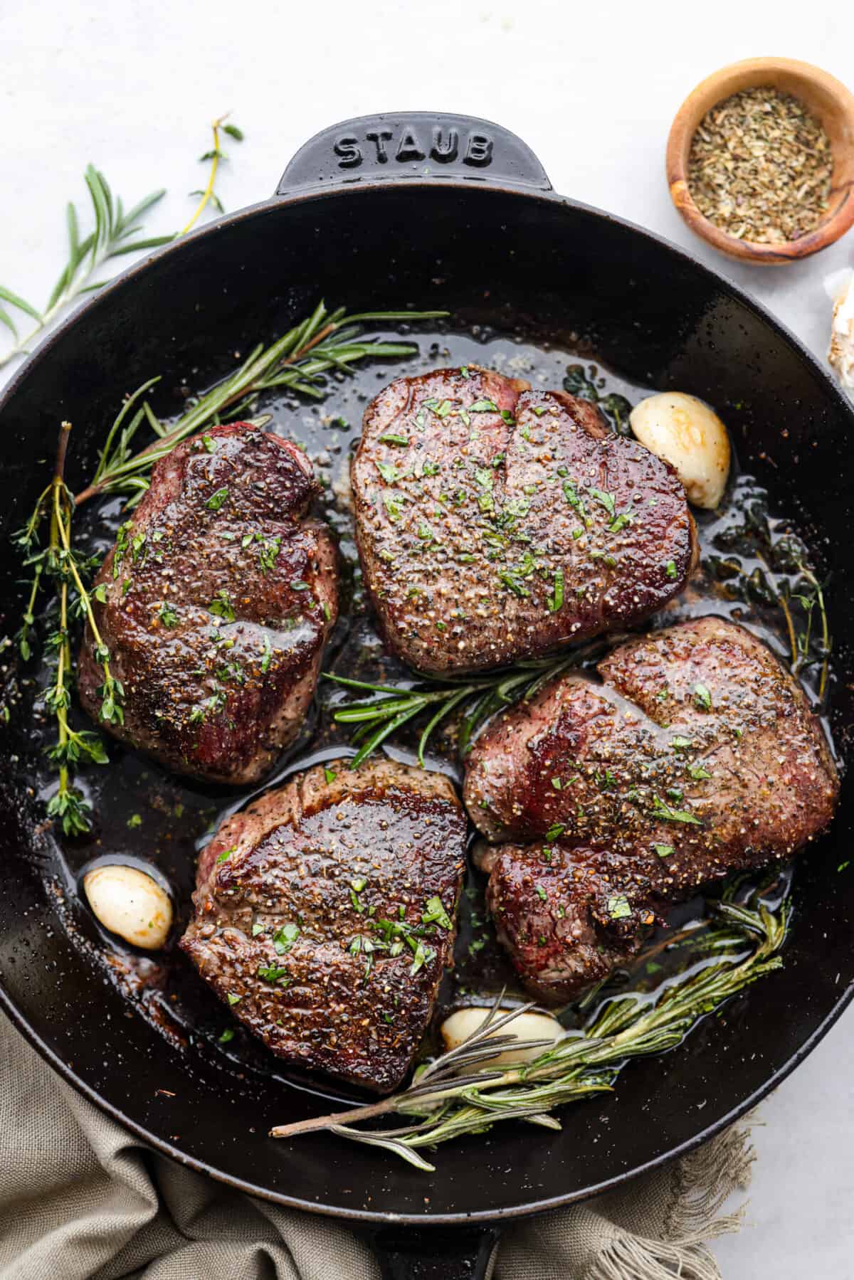 Top view of filet mignon in a black cast iron pan with garlic and herbs.