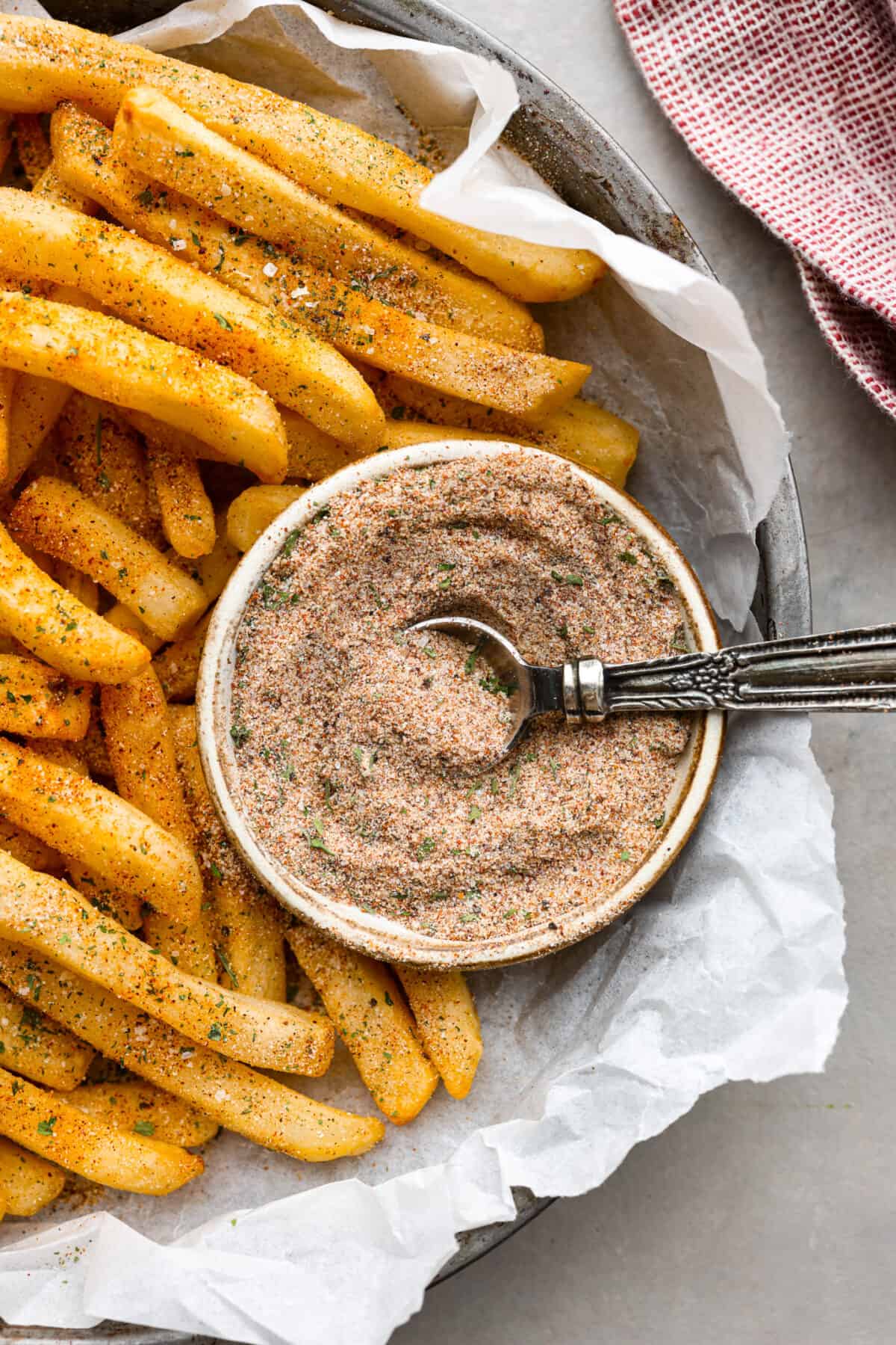 A bowl of fry seasoning in a tin with some French fries next to it. 