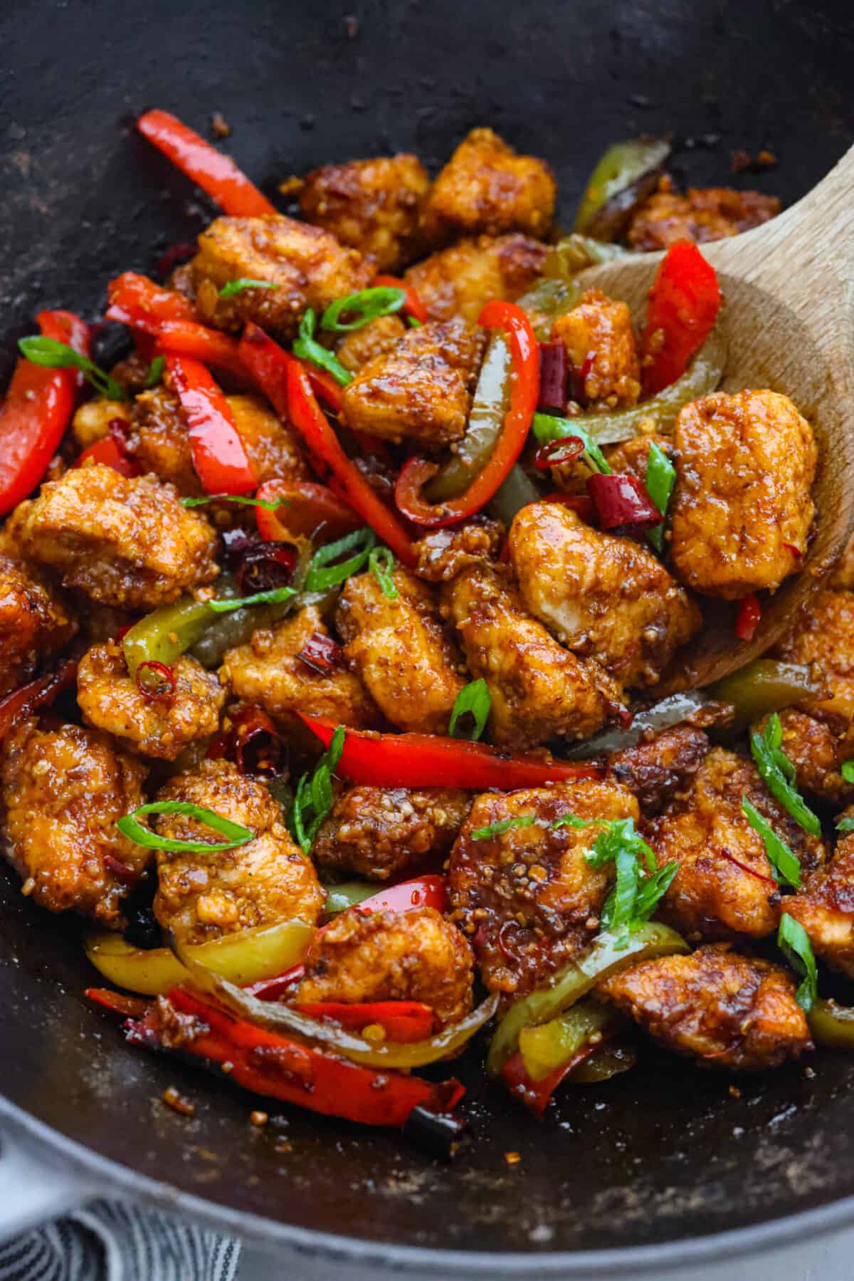 Closeup of kung pao chicken, being scooped up with a wooden spoon.