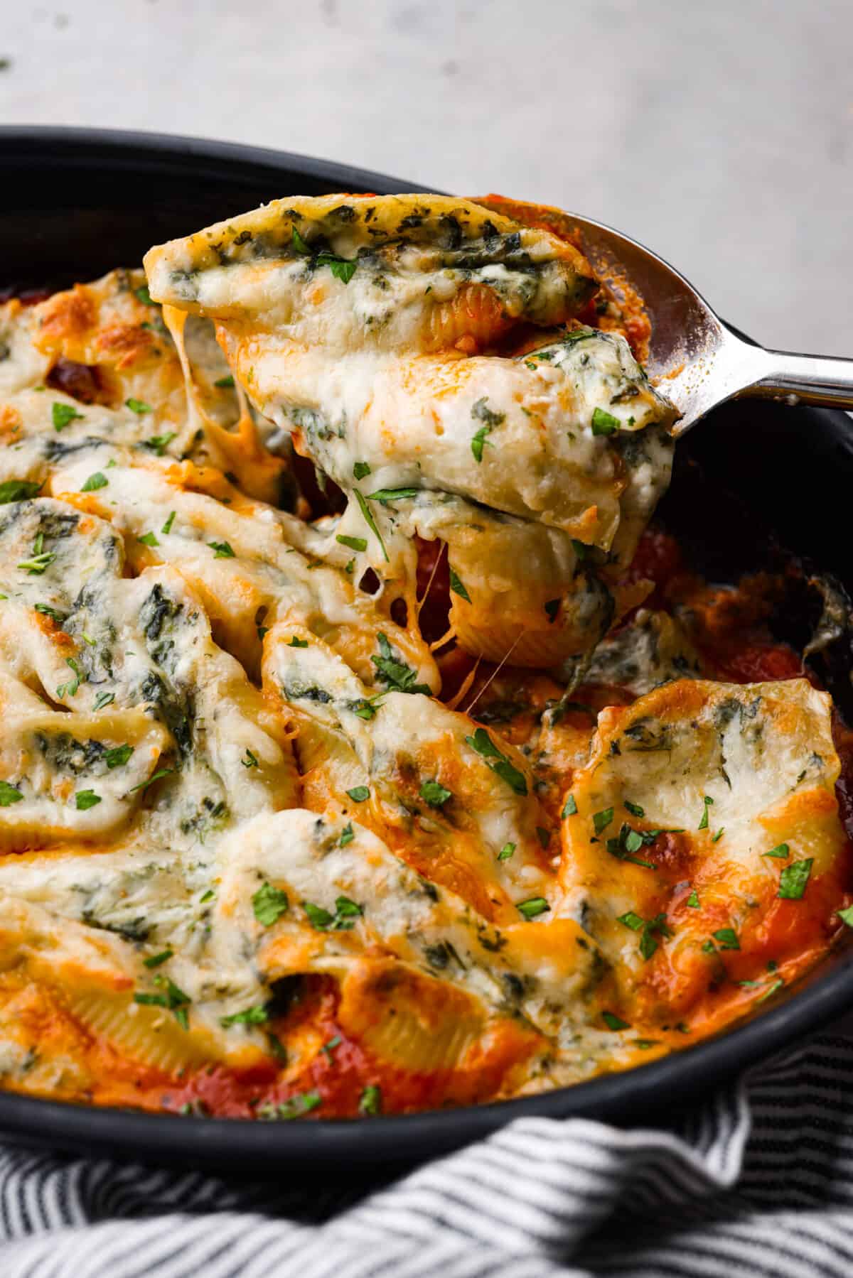 Closeup of spinach stuffed shells stuff scooped up with a large metal spoon.