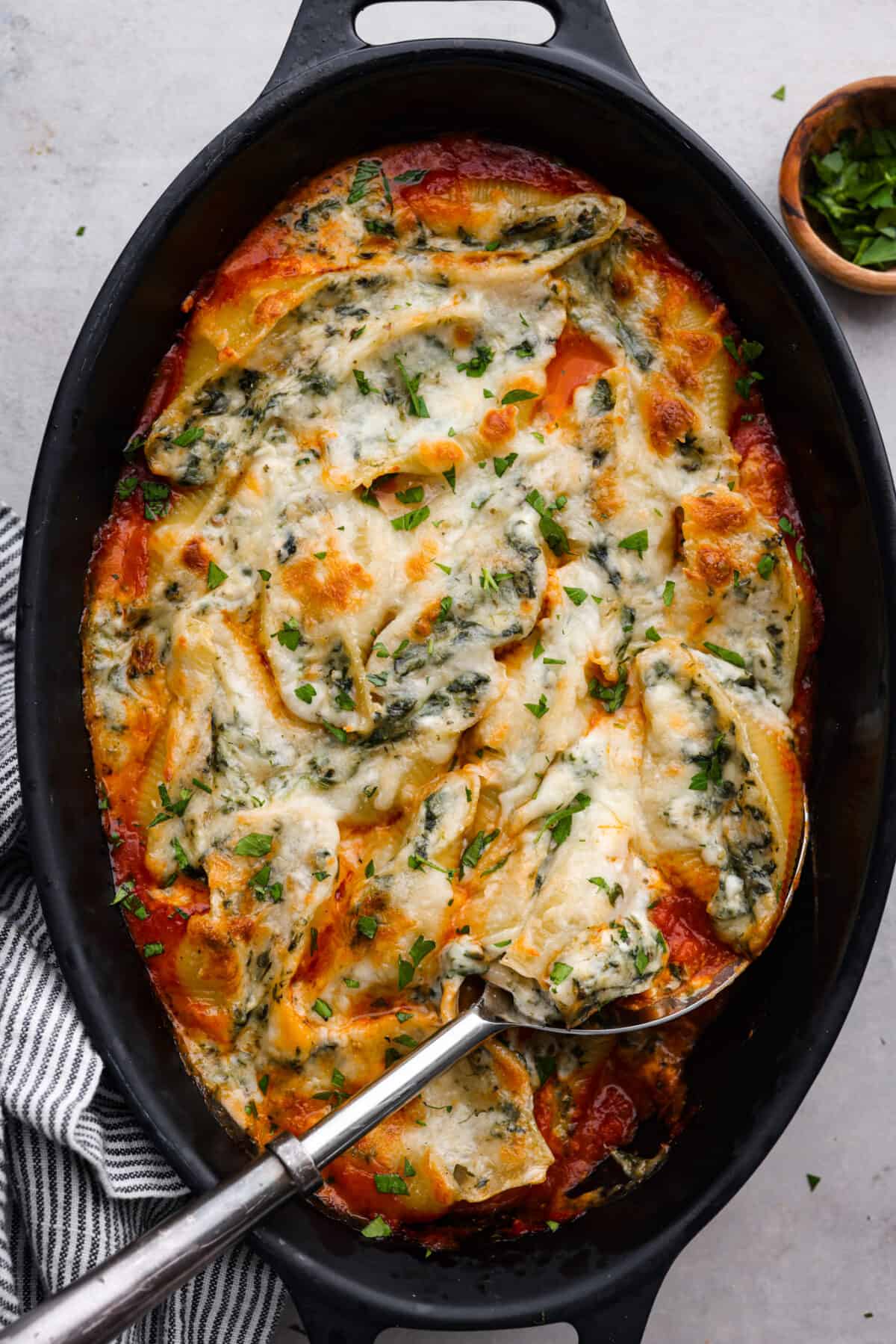 Top-down view of baked, stuffed shells in a black casserole dish.