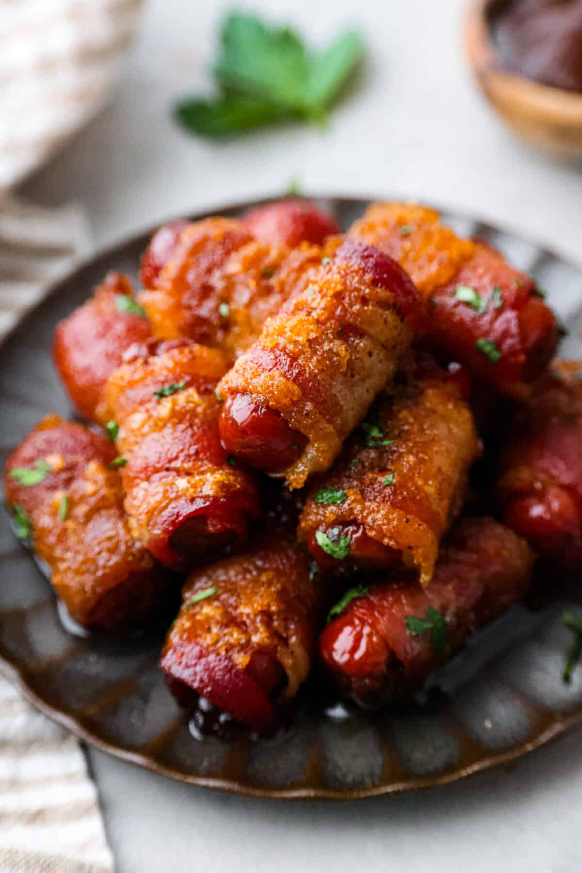 Close view of bacon wrapped smokies stacked on a brown plate.