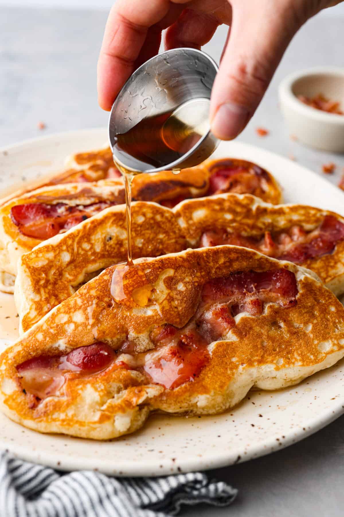 Pouring maple syrup over bacon pancakes.