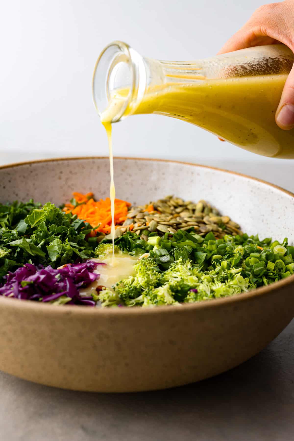 This healthy and colorful detox salad is LOADED with lots of greens and fresh veggies. The added nuts and seeds give a delicious crunch and texture to the salad. Drizzled with a lemon ginger vinaigrette, this salad has so many vibrant flavors! Side view of the dressing pouring over the salad ingredients.