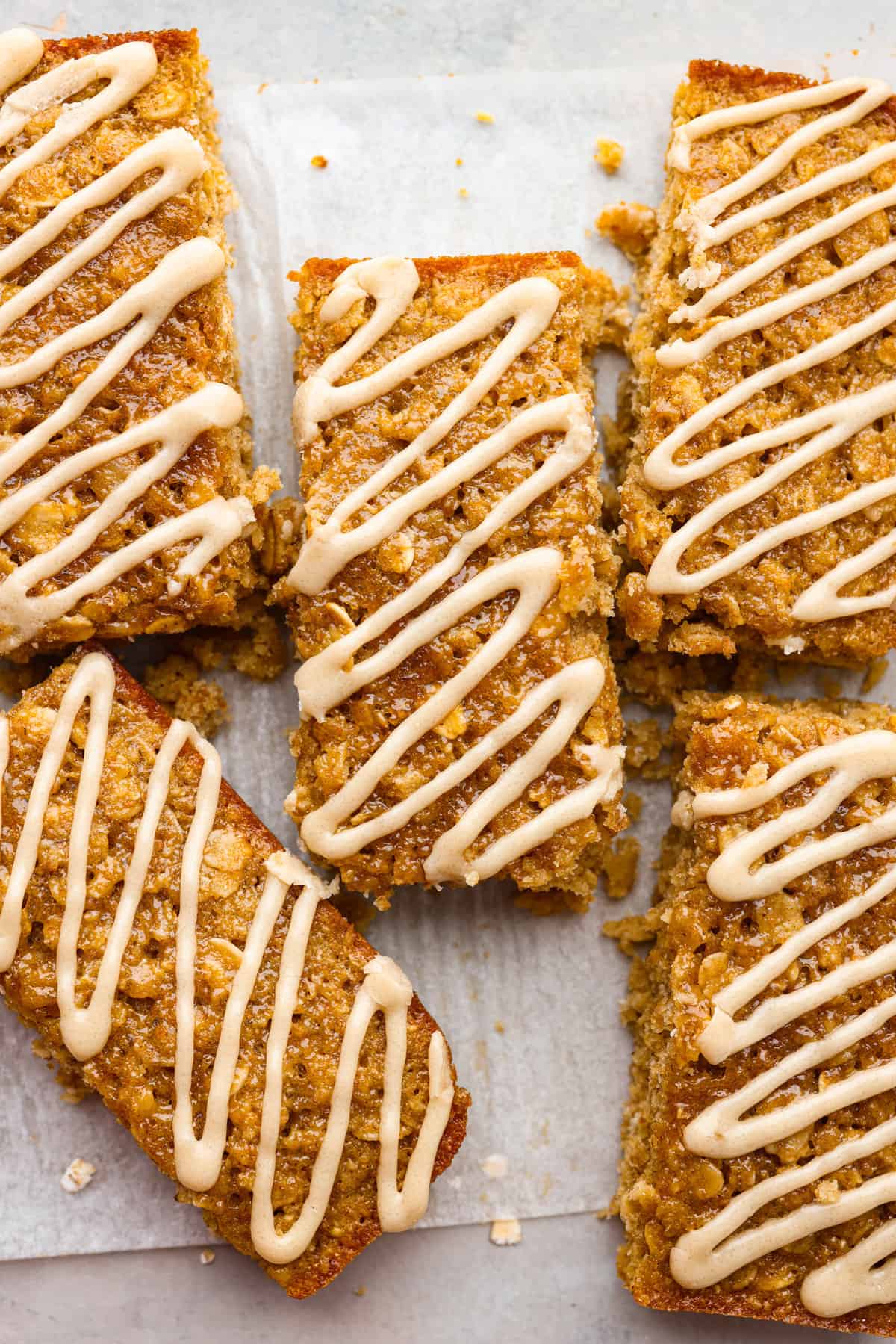 Start your day right with these simple and delicious Oatmeal Breakfast Bars. Topped with a sweet brown sugar maple glaze, these bars are easy to whip up and guaranteed to be a hit for a wholesome morning treat. A close up shot of breakfast bars with a glaze drizzled on them.