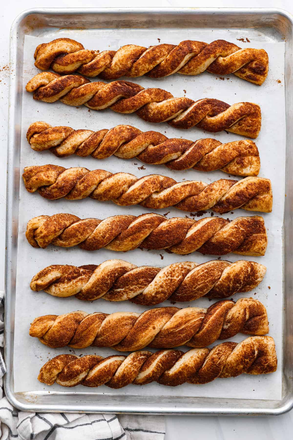 Everyone LOVES these sweet and fluffy cinnamon roll breadtwists. Homemade dough twisted and baked in brown sugar cinnamon goodness. It's like eating the middle of a cinnamon roll! Perfect for breakfast, enjoy as a snack, or delicious as a dessert. Top view of the bread twists baked on a baking sheet.