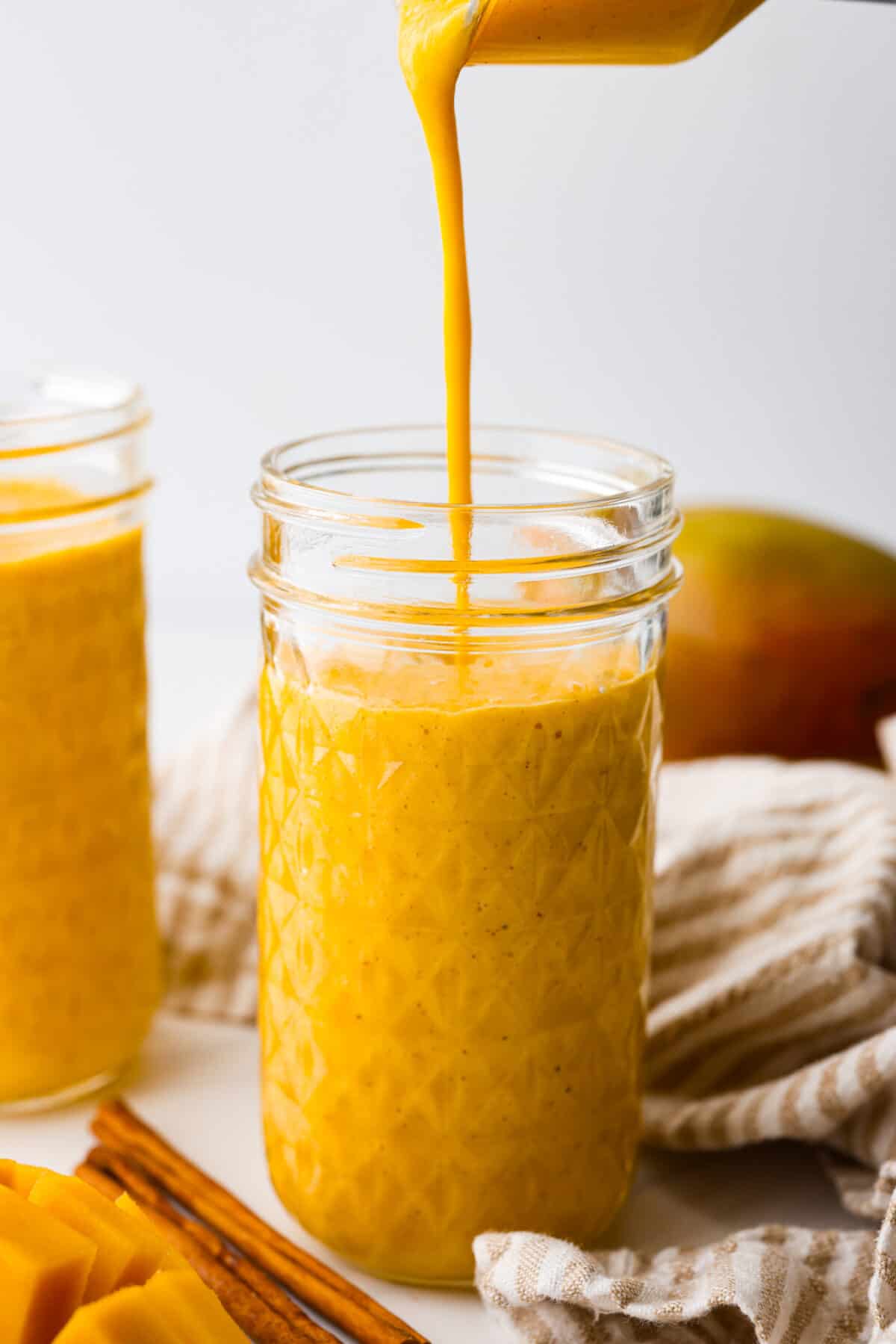 Close view of golden milk smoothie pouring into a tall glass jar. 