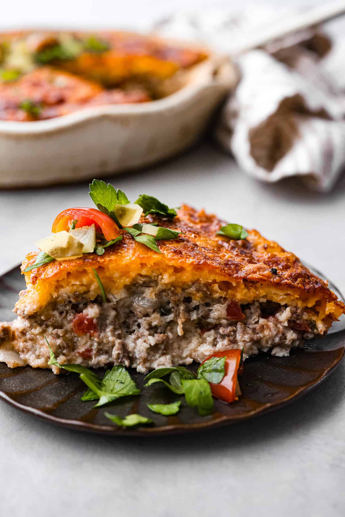 Impossible cheeseburger pie is an unexpected but TASTY twist on a cheeseburger! It's full of ground beef, and cheese, and the addition of Bisquick creates a comforting casserole texture. All your favorite hamburger ingredients are baked into a savory pie and your family will LOVE this version. Close view of a slice of cheeseburger pie on a plate.