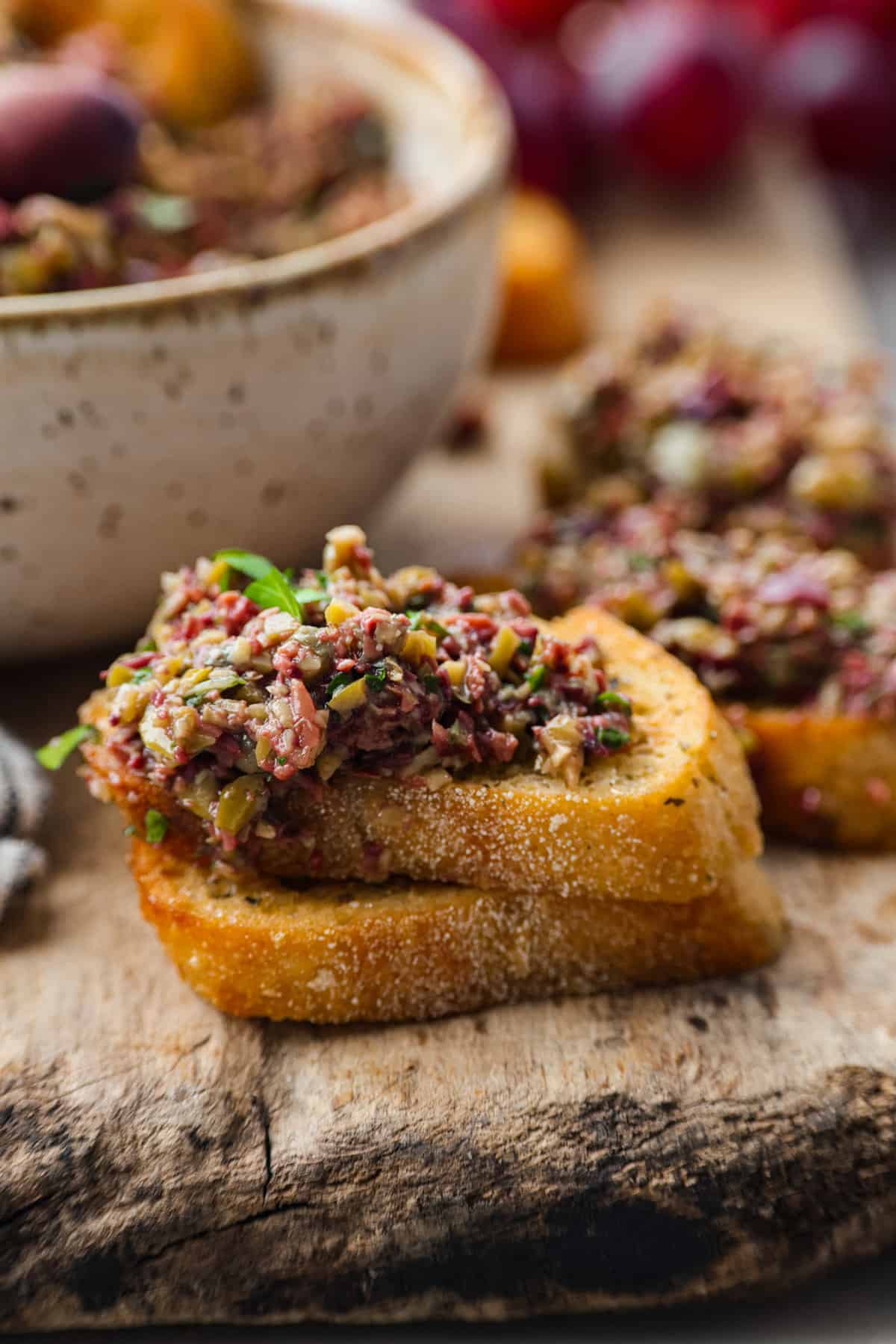 Impress your guests with the vibrant flavors in this easy olive tapenade. You'll love the combination of salty olives, capers, fresh herbs, and lemon to wake up your tastebuds. Enjoy as a spread, dip, or condiment...you will want it on everything! Close view of olive tapenade spread on crostini.