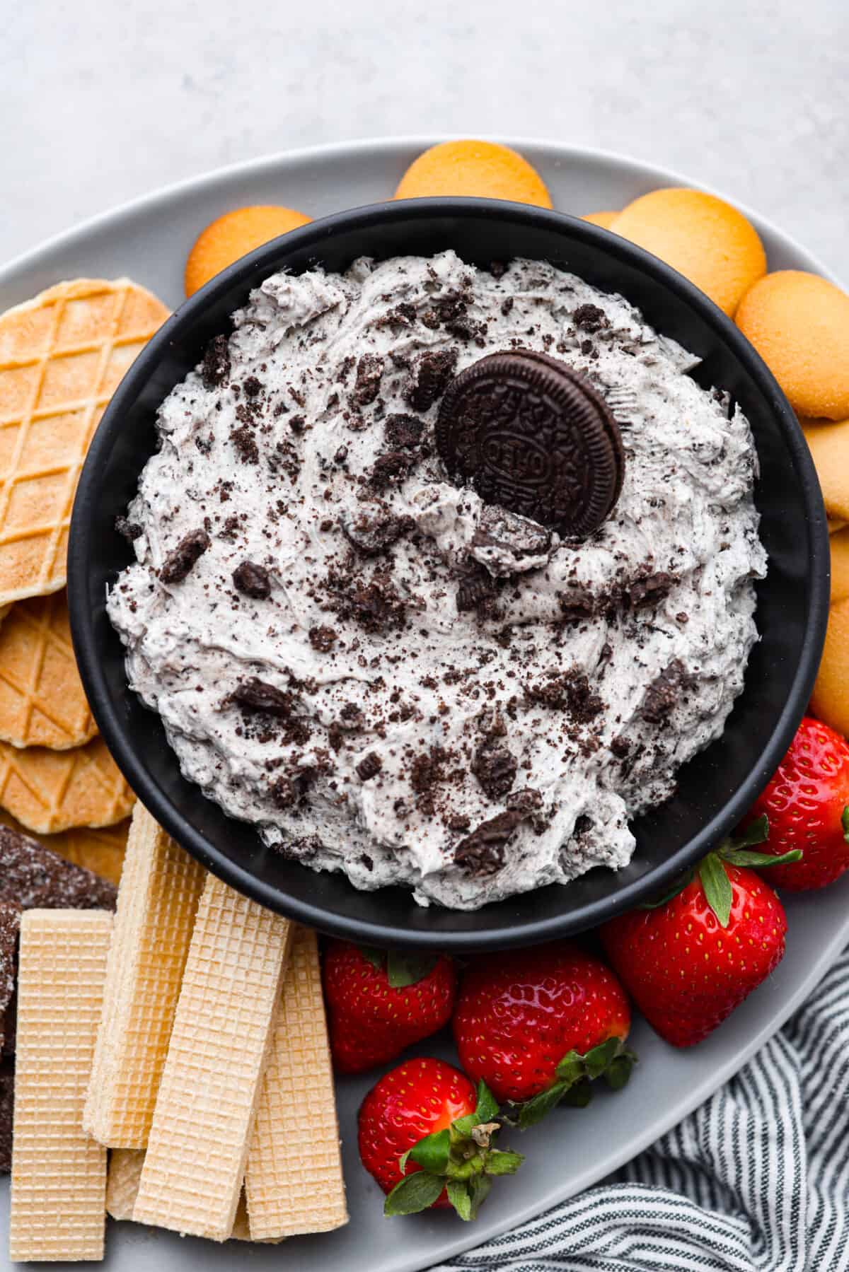A bowl of oreo dip surrounded by cookies, wafers, and strawberries.
