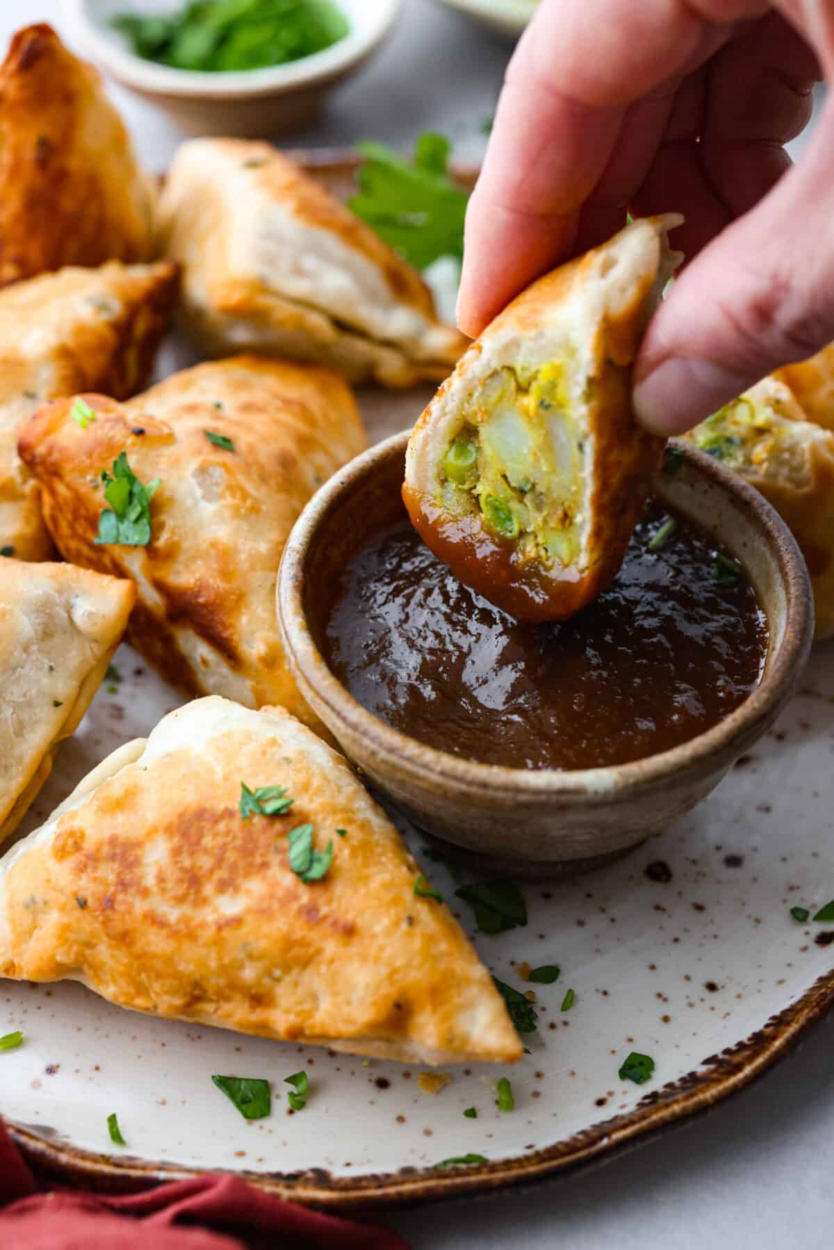 Close side view of a samosas appetizer dipping in a bowl of tamarind sauce. 