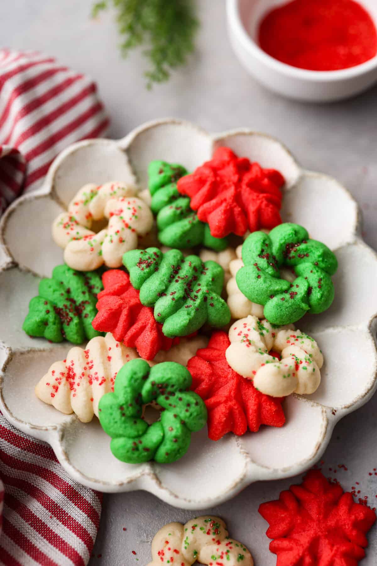 Red, green, and plain Spritz cookies in a white scalloped serving dish.
