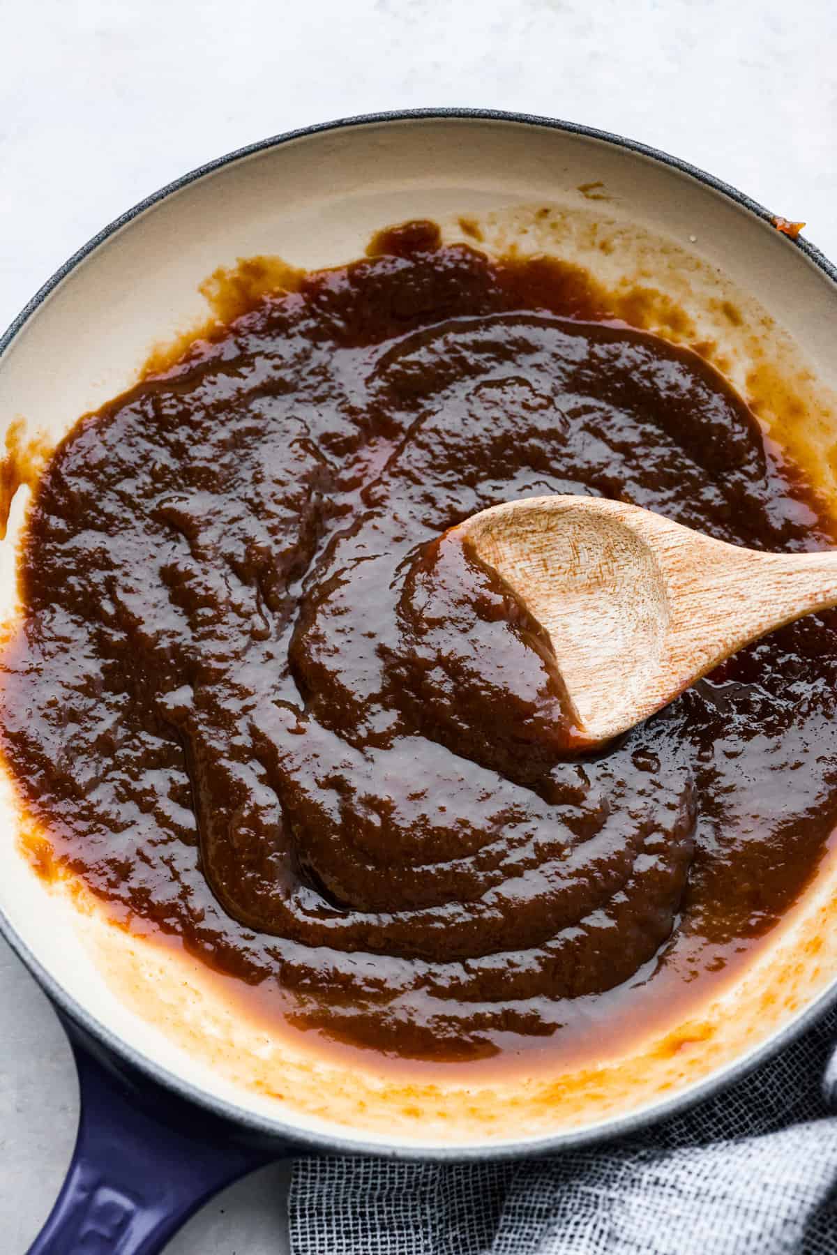 Tamarind sauce is a savory sweet and sour condiment used as a marinade, glaze, or for dipping appetizers. Make this versatile sauce at home and enjoy it with Thai and Indian cuisine. Top view of tamarind sauce in a saucepan with a wood serving spoon.