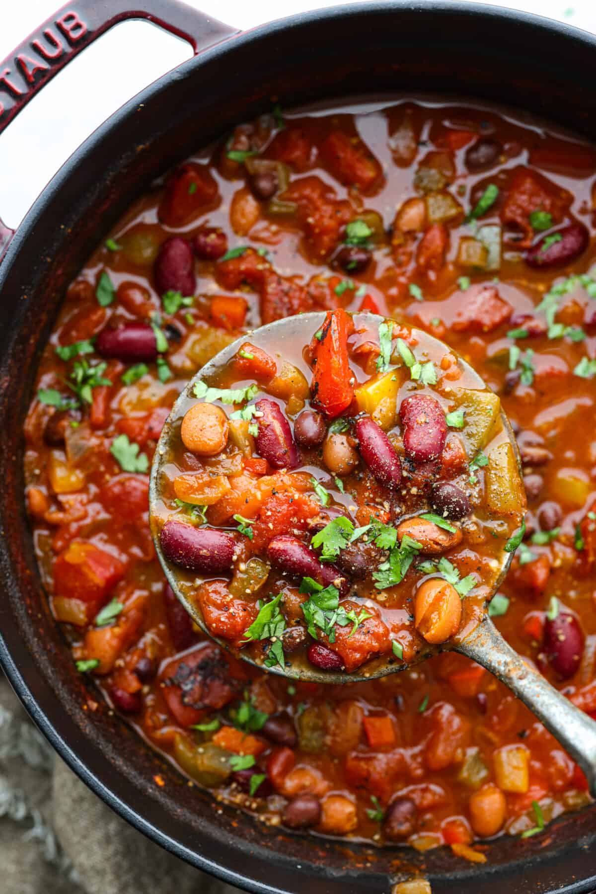 Close overhead view of vegetarian chili in a large pot. A ladle is lifting up a scoop of chili.
