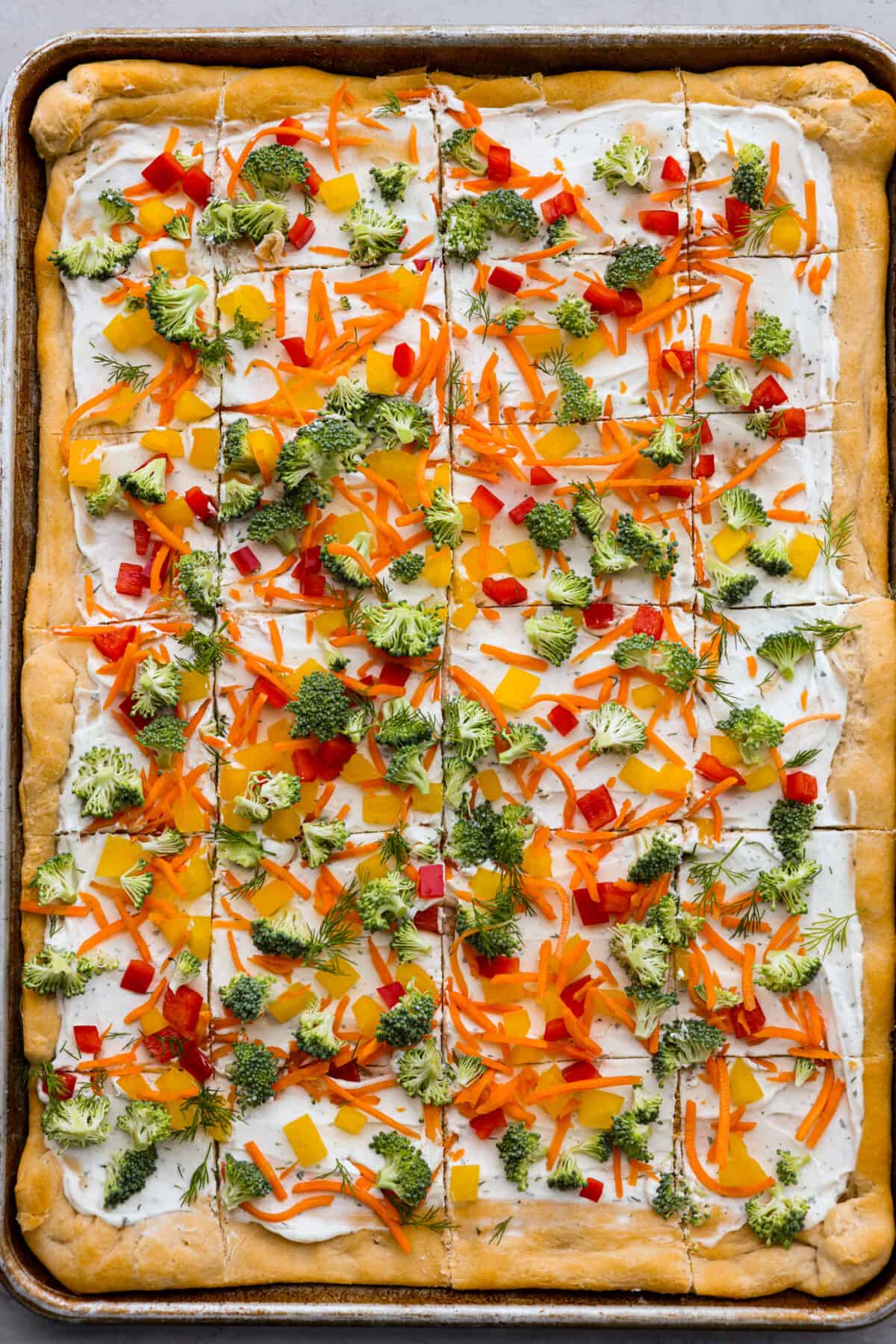 A whole vegetable pizza made from crescent roll dough, a creamy ranch spread, broccoli, shredded carrots, chopped dill, and bell peppers.