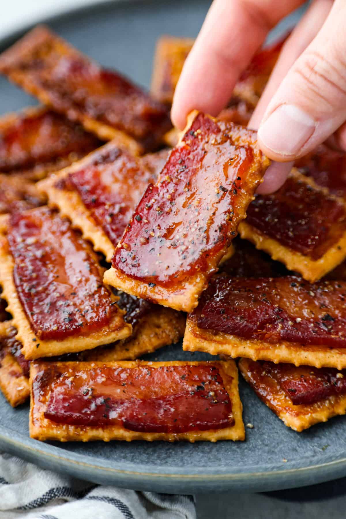 Close view of a hand holding up a bacon cracker from a plate of stacked crackers.