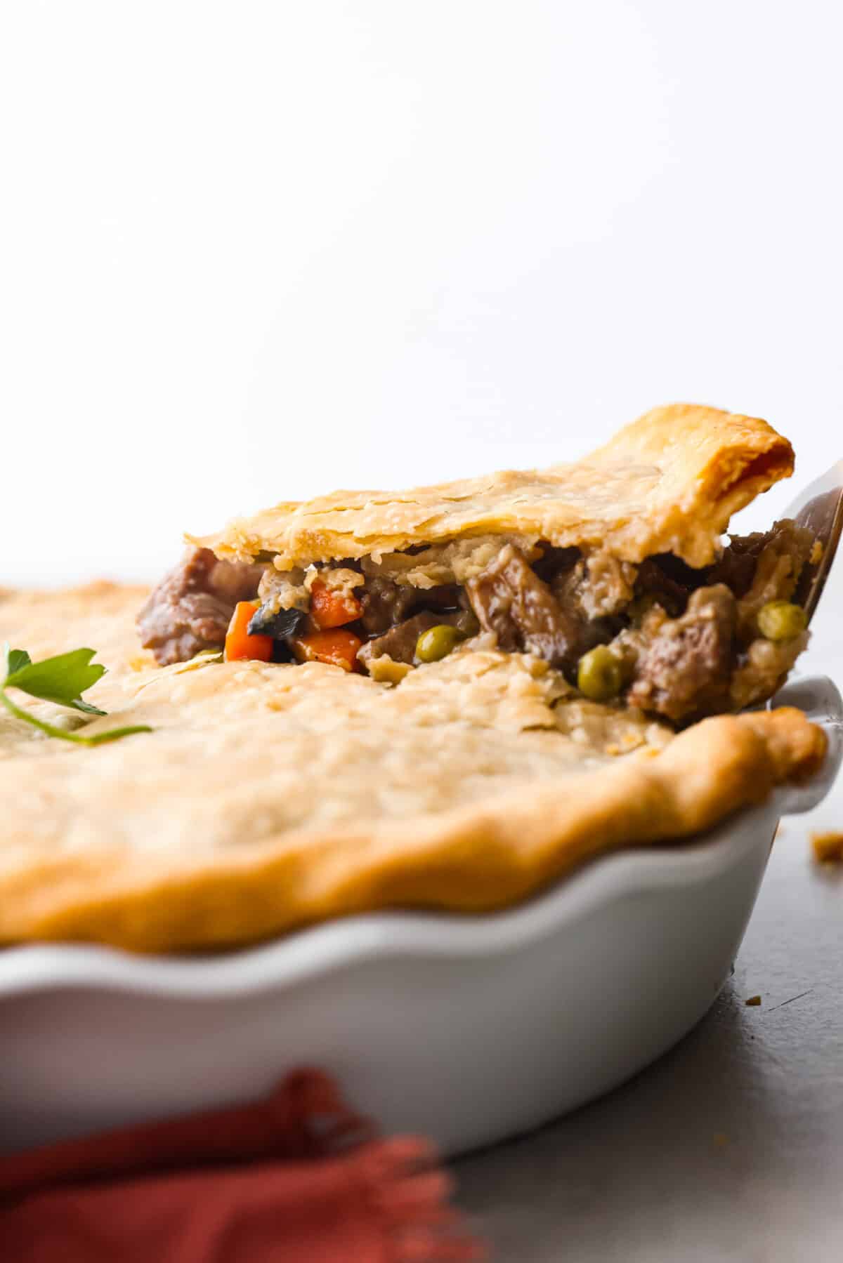 Lifting a piece of beef pot pie out of a baking dish.