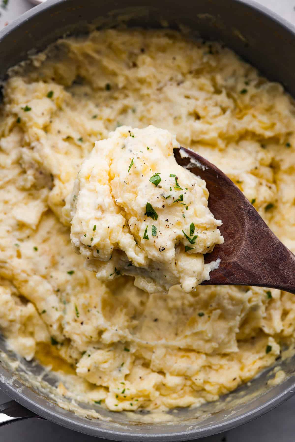 Decadent Boursin mashed potatoes are incredibly creamy and perfectly seasoned. Level up your mashed potatoes with butter, heavy cream, and the addition of Boursin cheese, a soft gourmet cheese. Close view of a wood serving spoon lifting a the mashed potatoes.