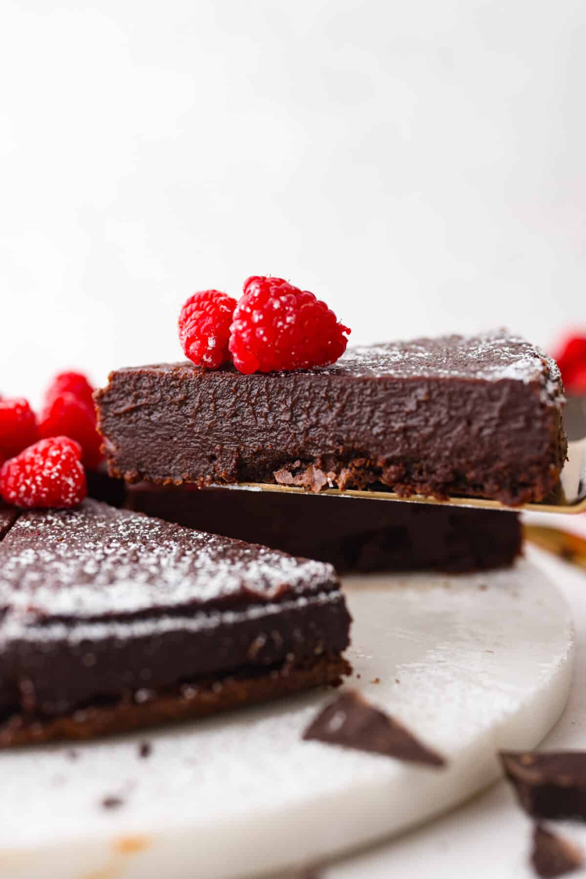 A slice of chocolate cake being served with a cake spatula. There are raspberries on top of the cake.