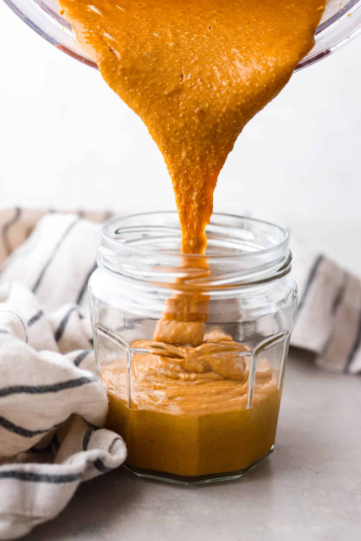 Pouring peanut butter into a glass jar.