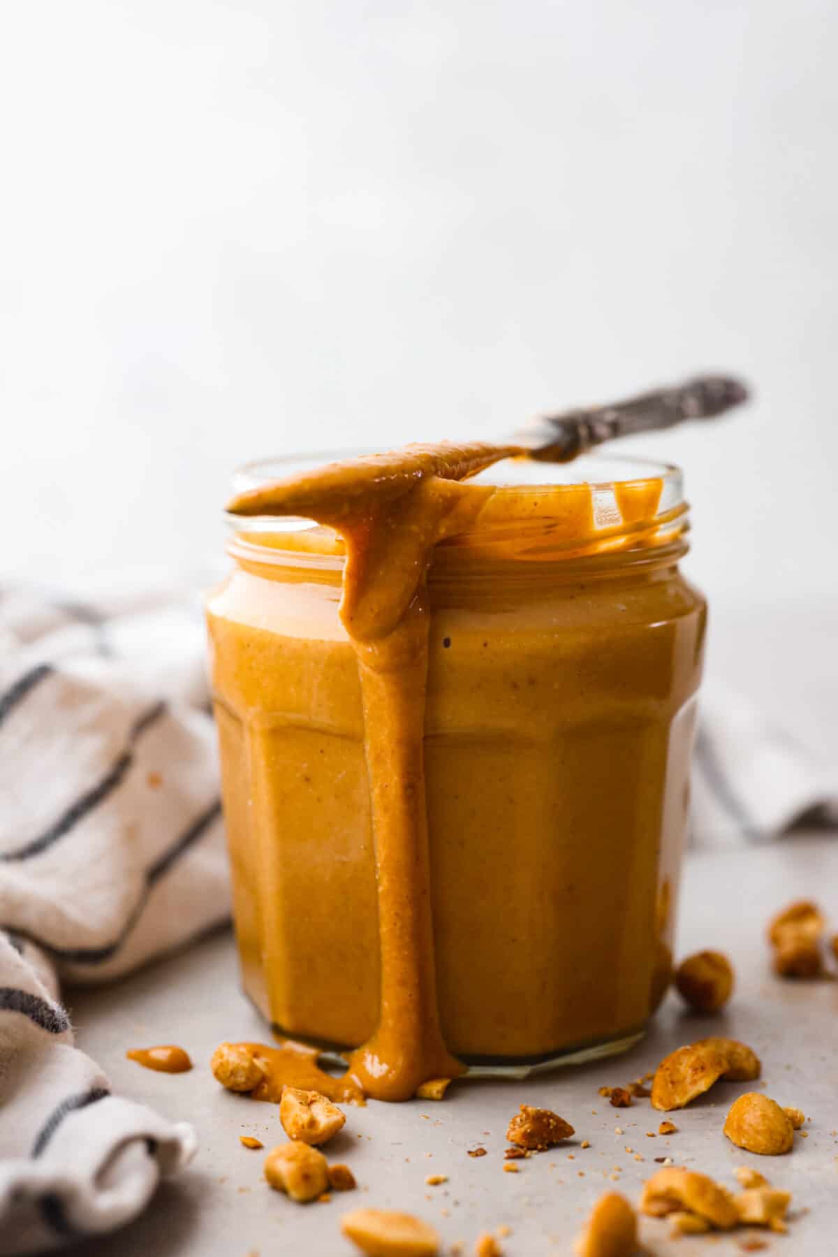 A glass jar filled with peanut butter, topped with a metal butter knife that also has peanut butter on it.
