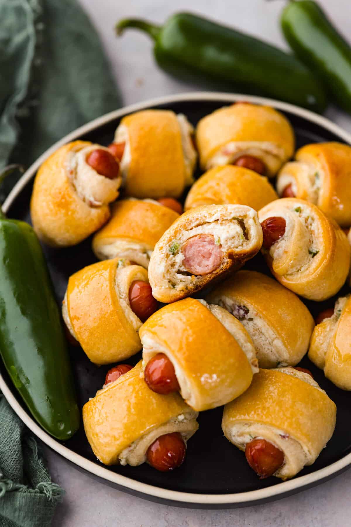 Close view of jalapeno popper pigs in a blanket stacked on a black plate with a bite out of one.