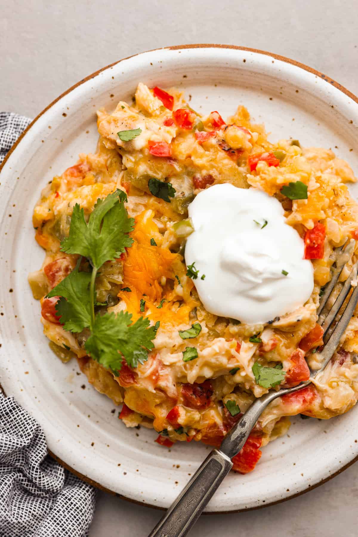 King Ranch Casserole is your solution if you're looking for a dinner that is both delicious and easy to make! It's a creamy dish with layers of chicken, cheese, and tortilla chips that your family is going to want on repeat. Top view of a serving of king ranch casserole on a plate garnished with cilantro and sour cream.