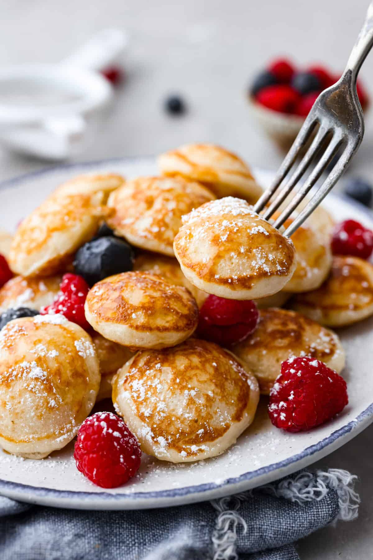 Closeup of small Dutch pancakes served with berries and powdered sugar.