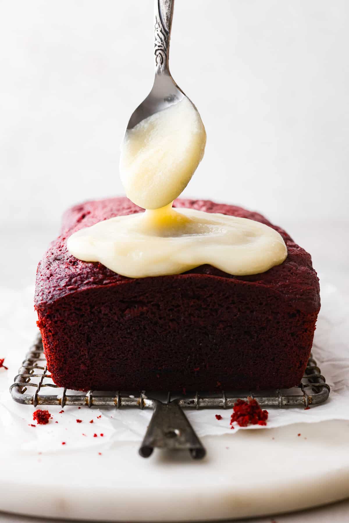Fall in love with this perfectly moist red velvet pound cake with a cream cheese glaze! With its signature red color and the subtle chocolate flavor, this pound cake is easy to make and irresistibly delicious! Close side view of the cream cheese glaze drizzling on top of the red velvet pound cake.