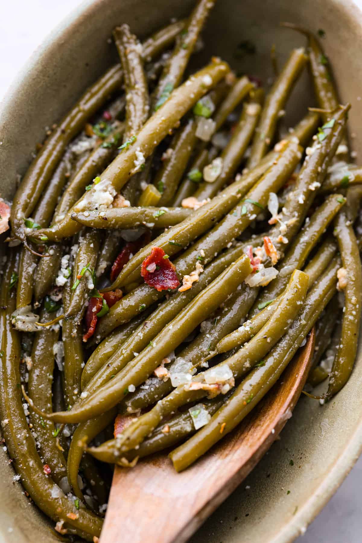 These Crockpot Green Beans are perfectly tender, packed with flavor and so easy to cook in your slow cooker. All you need is 5 minutes of prep time to have a side dish that pairs well with almost any meal! Scooping up the green beans with a wooden spoon.