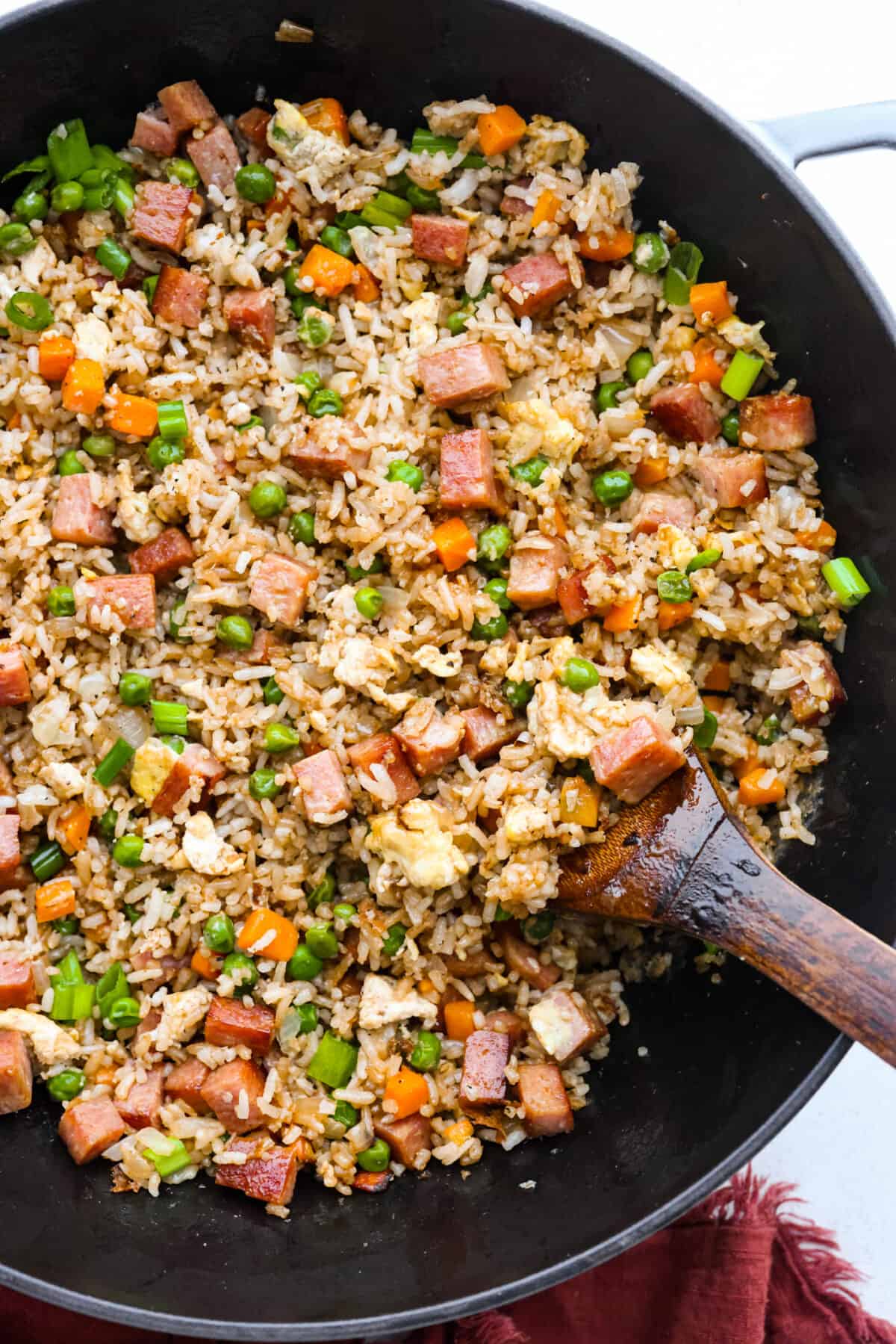 Spam fried rice in a wok, being stirred with a wooden spoon.