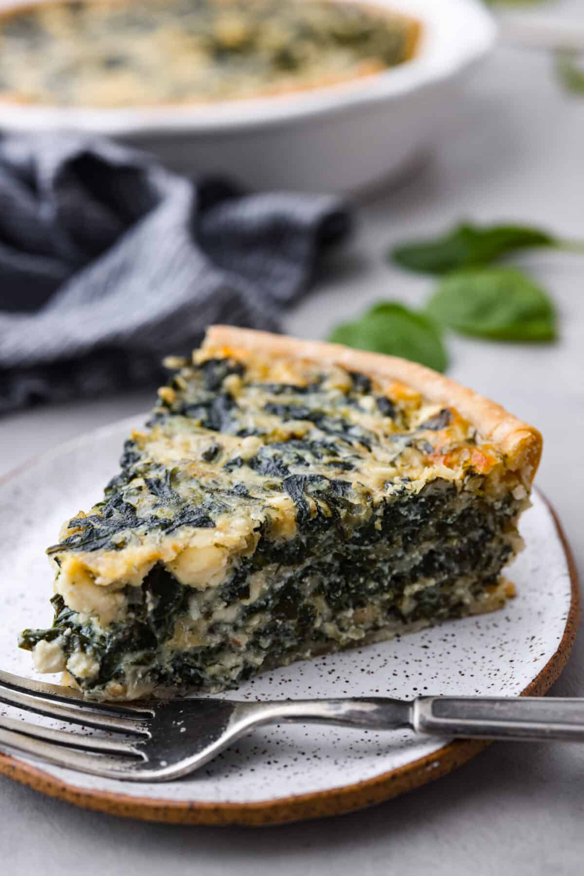 Close view of a slice of spinach pie on a small white plate with a fork.