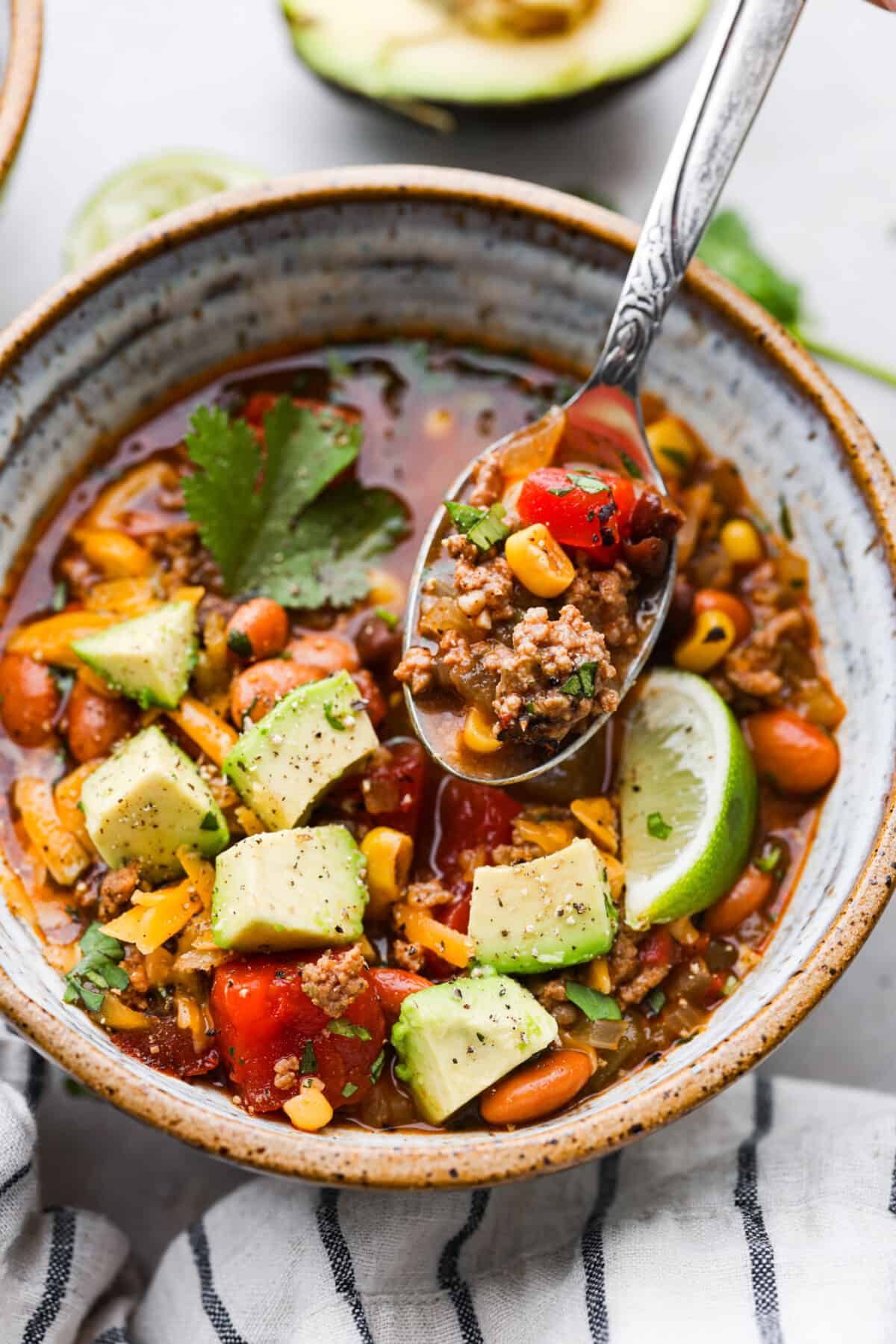 Closeup of a serving of taco soup, with ground beef, broth, and vegetables in a metal spoon.
