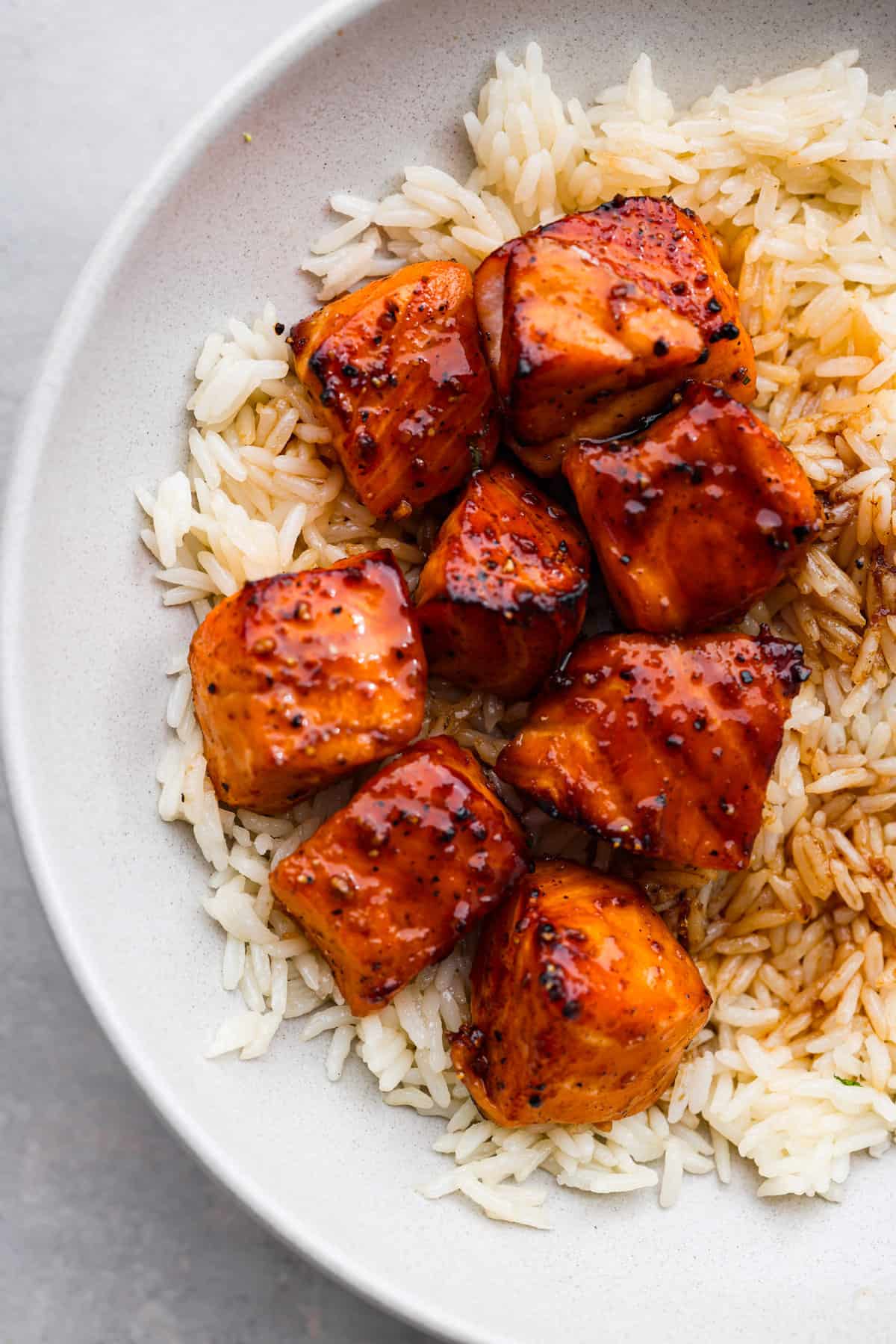 Say hello to your new favorite lunch: this honey-glazed salmon bowl made with juicy air fryer salmon bites, broccoli, and shredded carrots over white rice! Closeup of the salmon bites.
