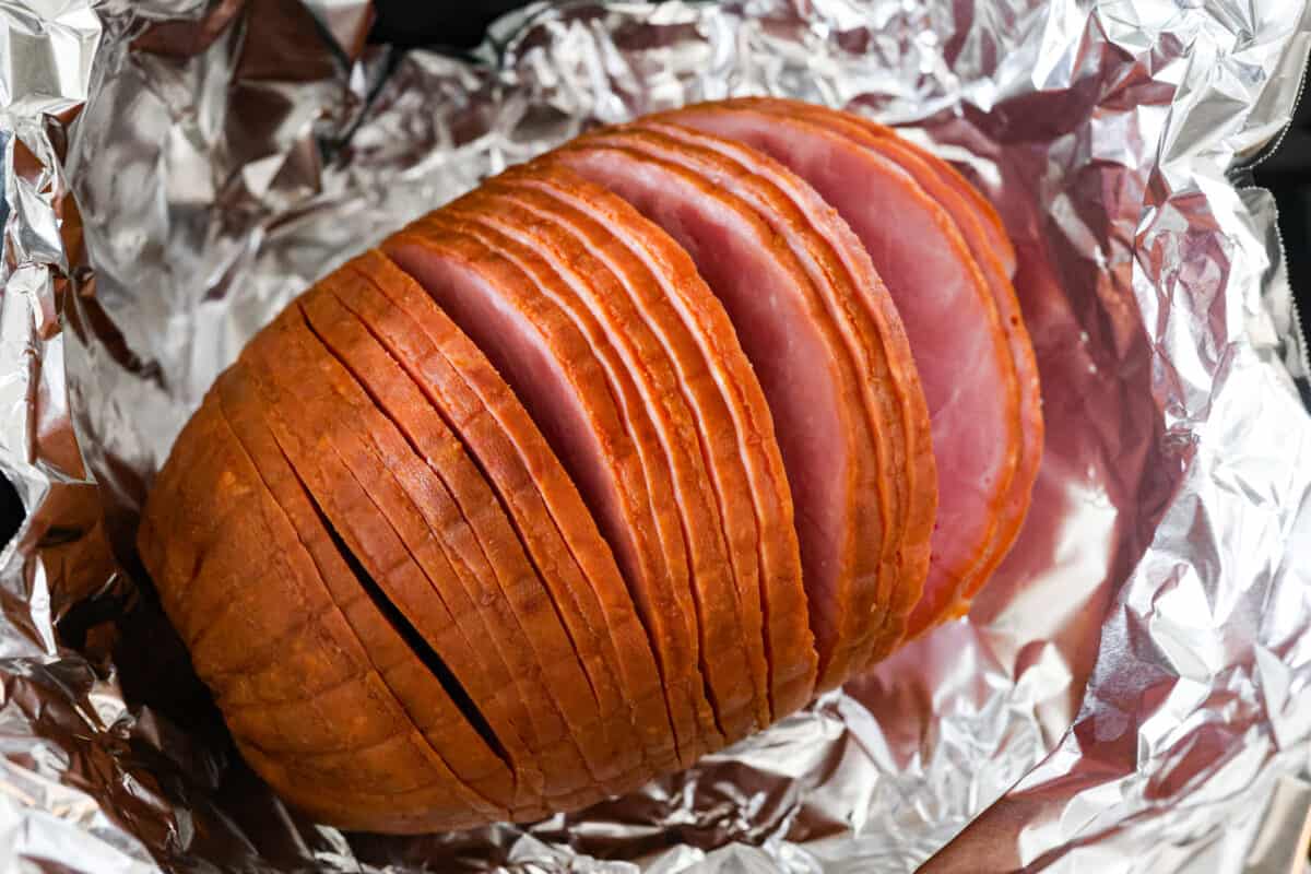 Adding the sliced ham to an aluminum foil-lined air fryer basket.