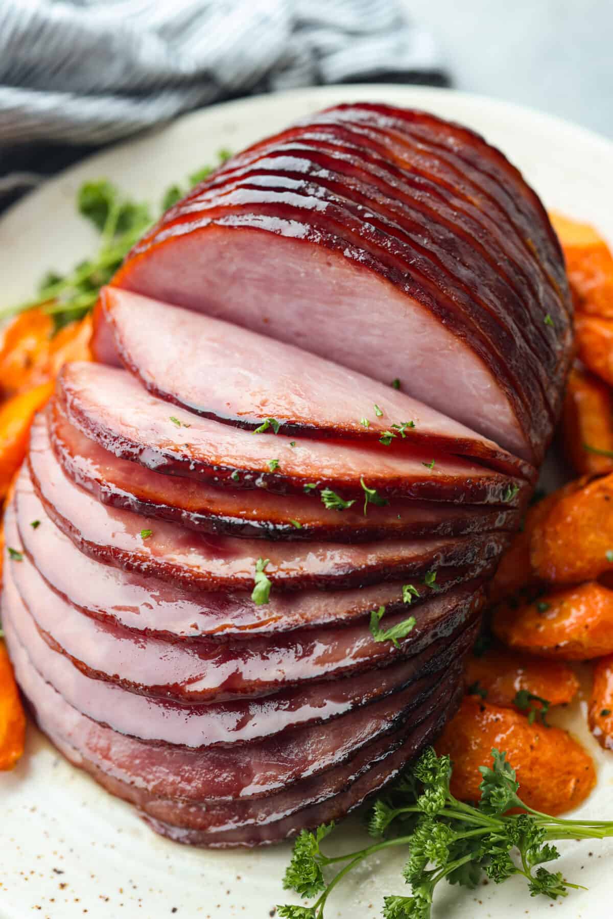 Closeup of a cut ham after being cooked in the air fryer. It is surrounded by sliced carrots.