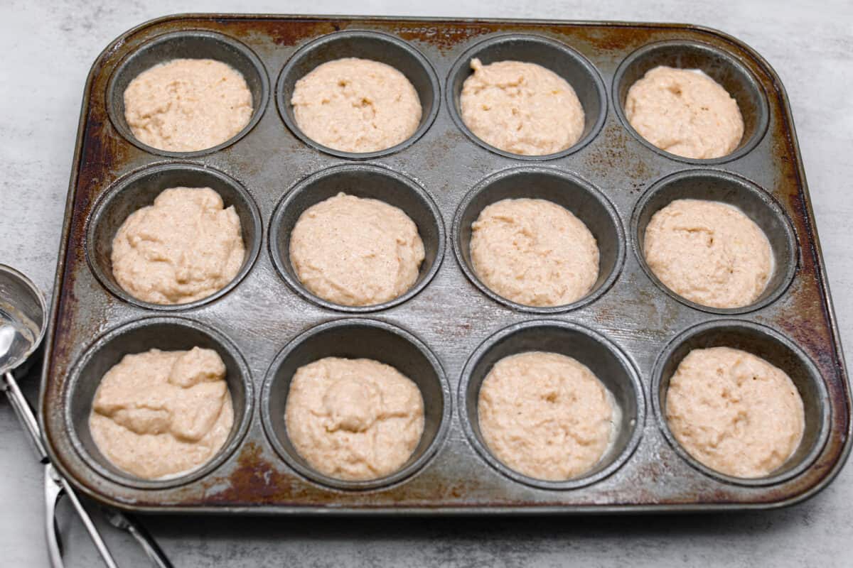 The applesauce muffin batter being added to a muffin tin.