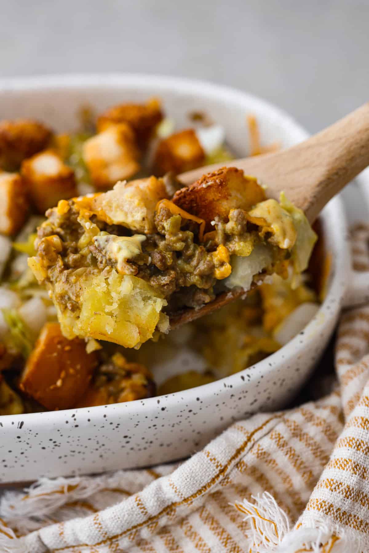 Meaty, cheesy, and chock full of tasty mix-ins like hash browns, pickles, and onions, Big Mac casserole is the perfect dinner to make this week! It’s an easy, deconstructed version of the classic burger we all know and love. A scoop of casserole on a wooden spoon.